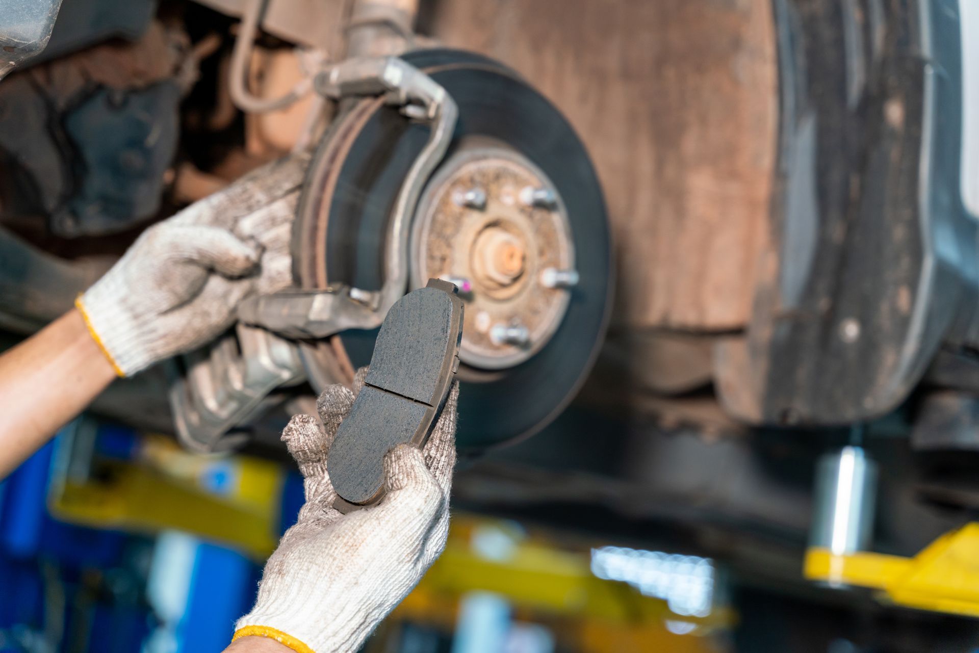 Gloved mechanic replacing a car brake pad on a lifted vehicle wheel hub. Gloved mechanic replacing a car brake pad on a lifted vehicle wheel hub.