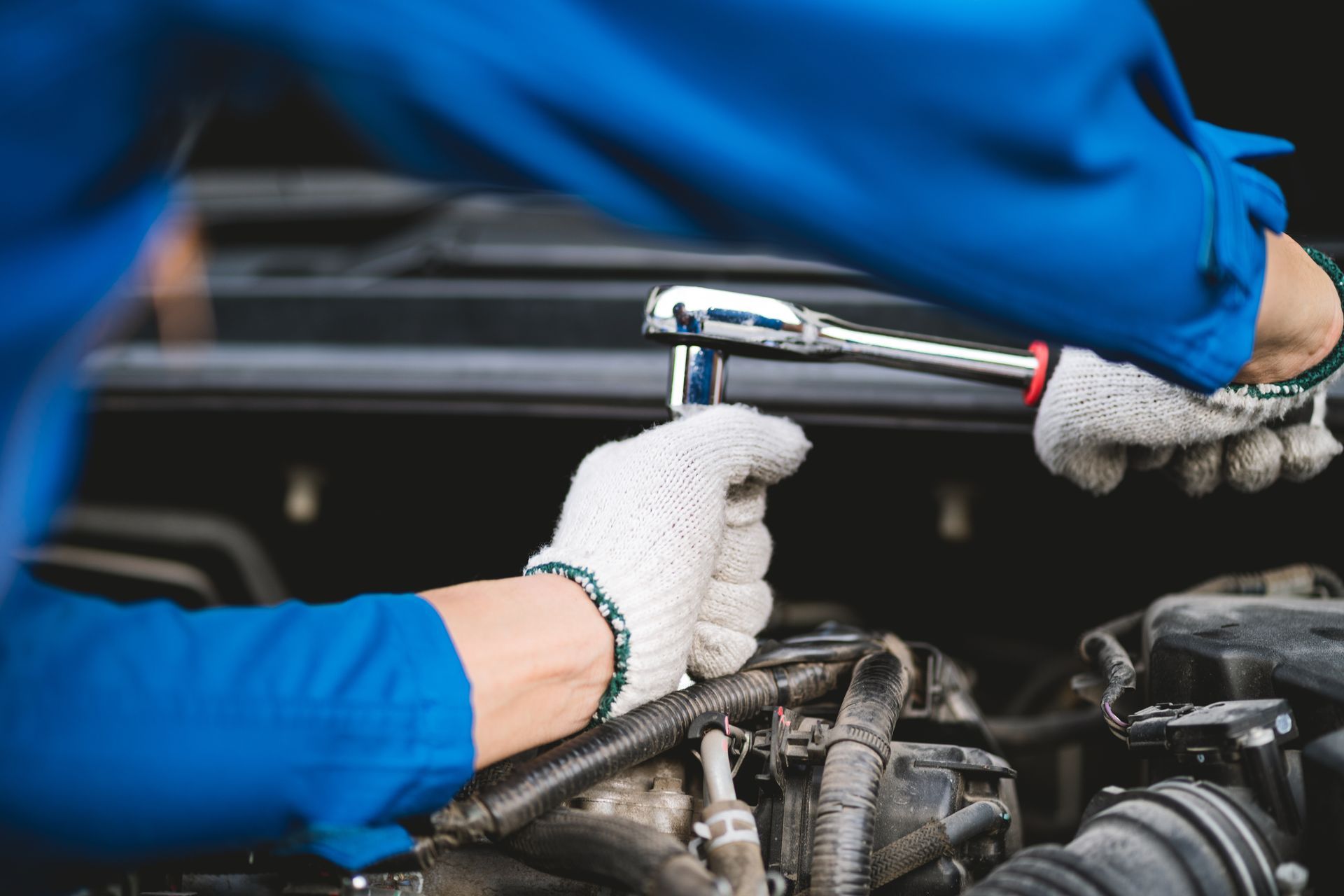 Gloved hands using a ratchet wrench to repair an engine in a car engine bay Gloved hands using a ratchet wrench to repair an engine in a car engine bay
