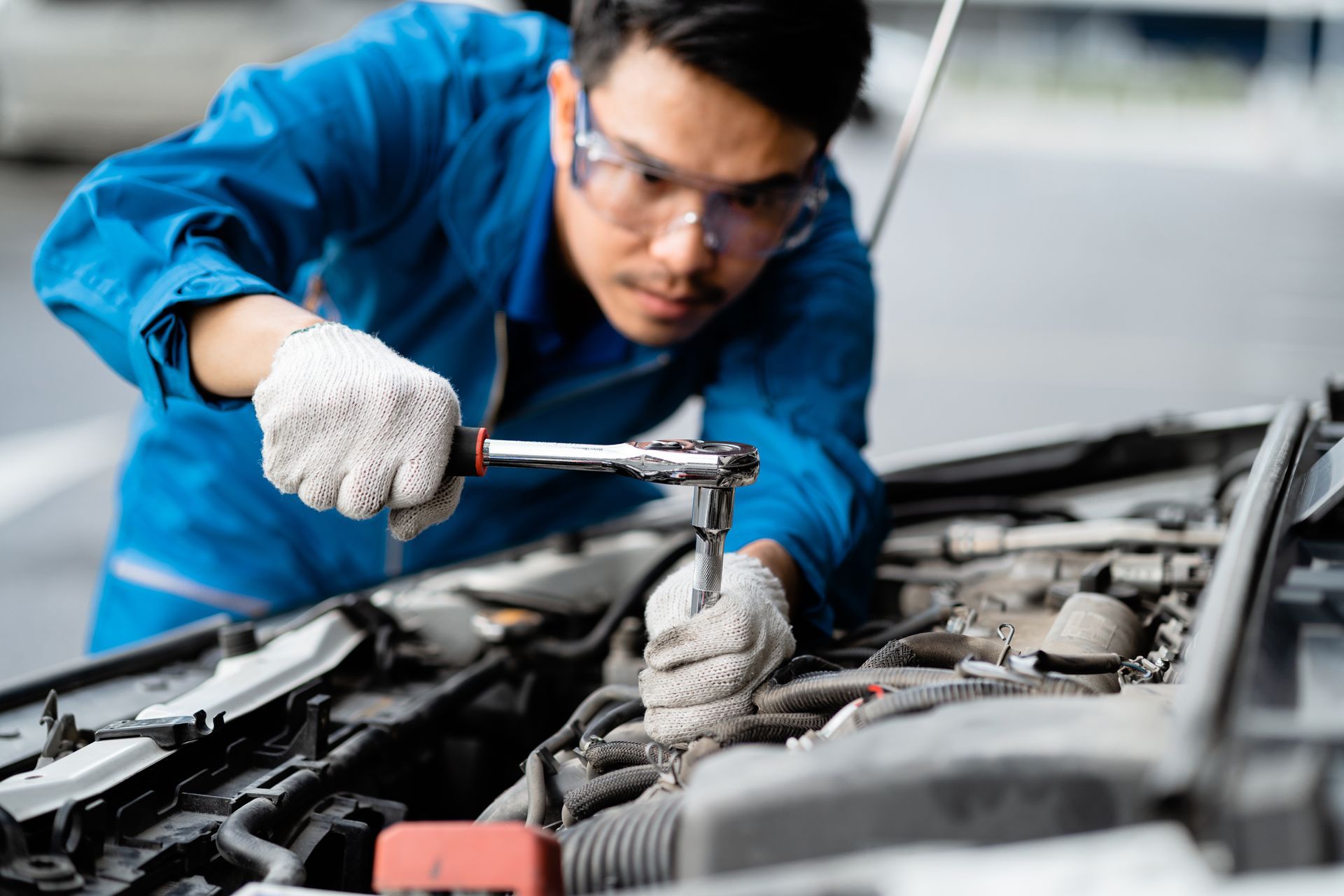 Mechanic in blue coveralls tightening a wrench in an open car engine bay