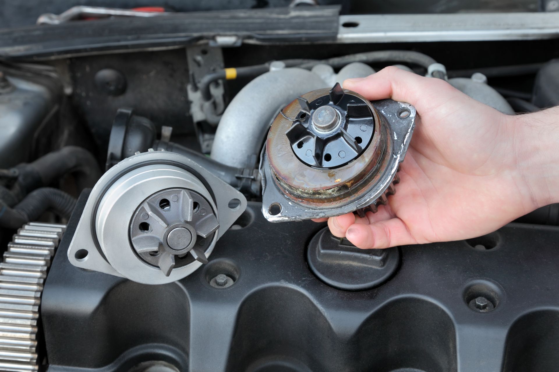 Hand holding a worn automotive part beside a metal replacement part in an engine bay Hand holding a worn automotive part beside a metal replacement part in an engine bay