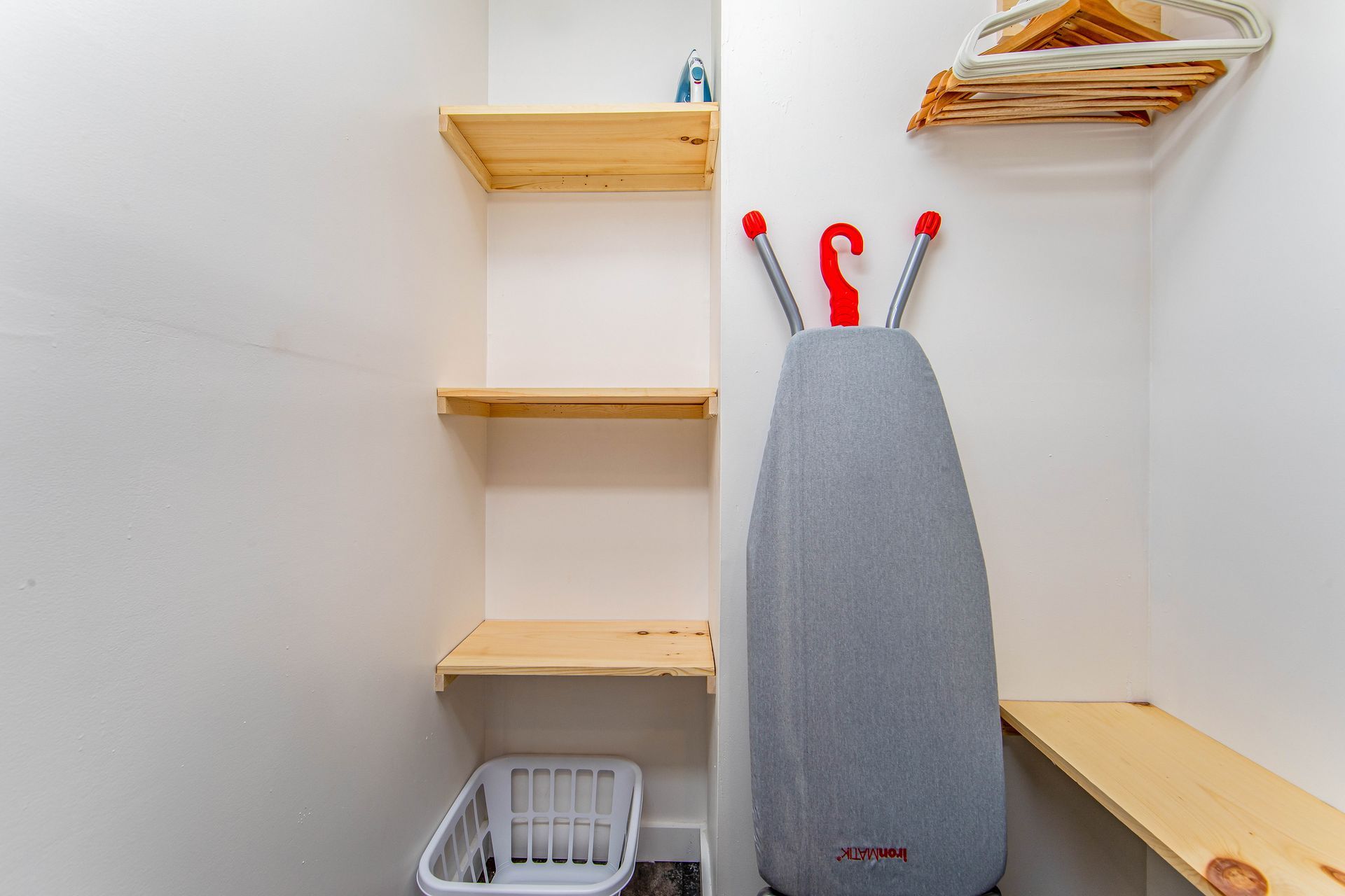 A laundry room with a ironing board and a basket.