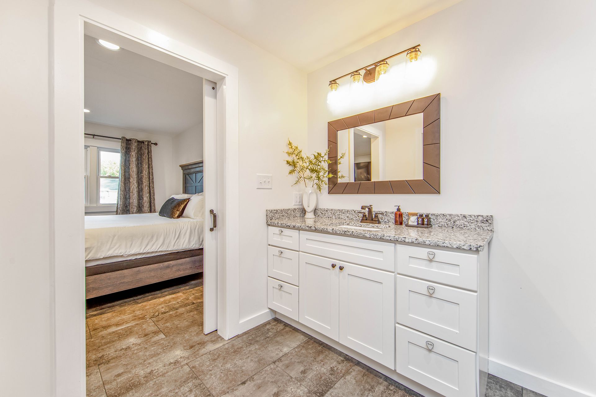 A bathroom with two sinks , a mirror and a door leading to a bedroom.