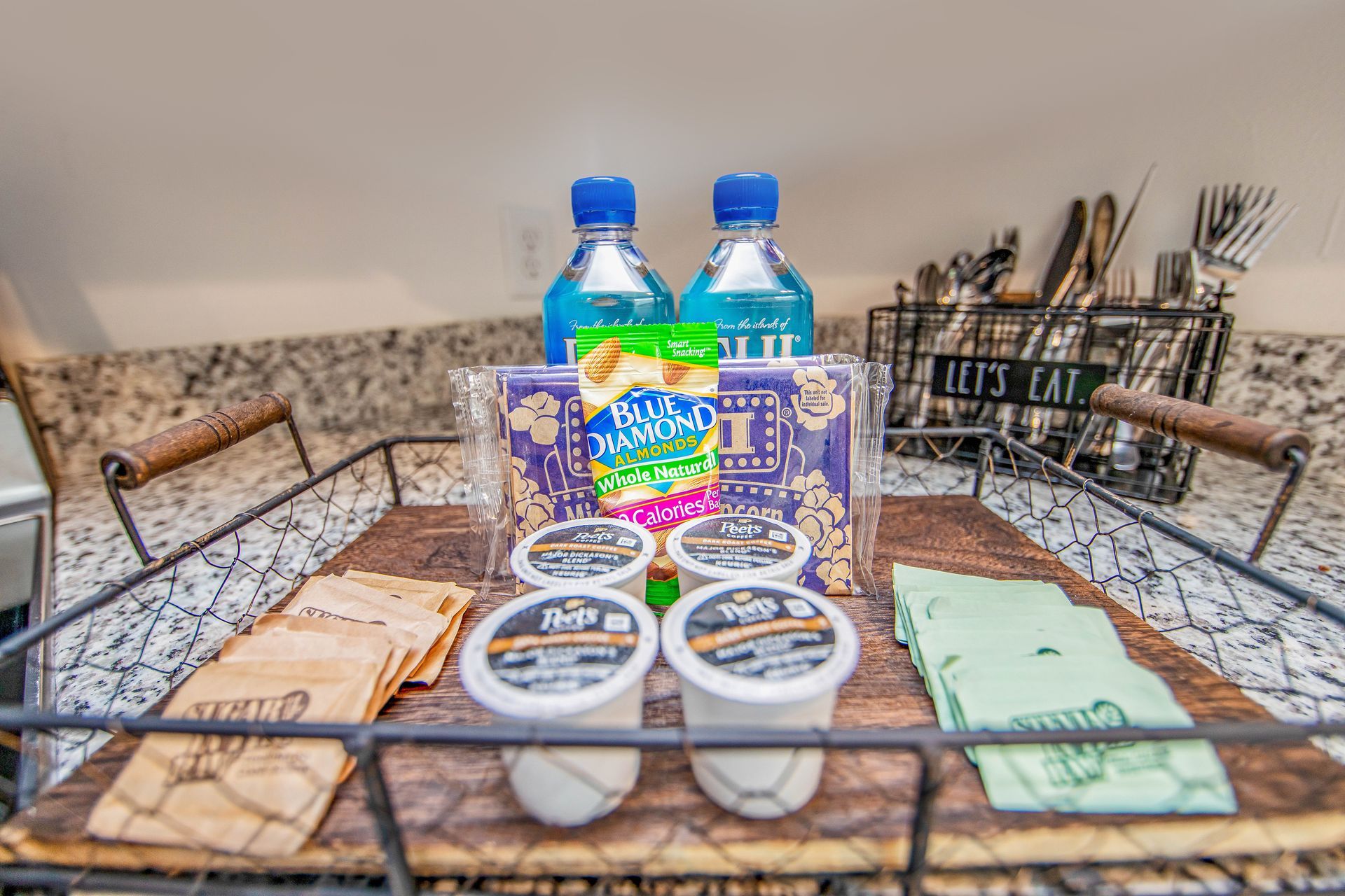 A wooden tray with bottles of water , popcorn , and yogurt on a counter.