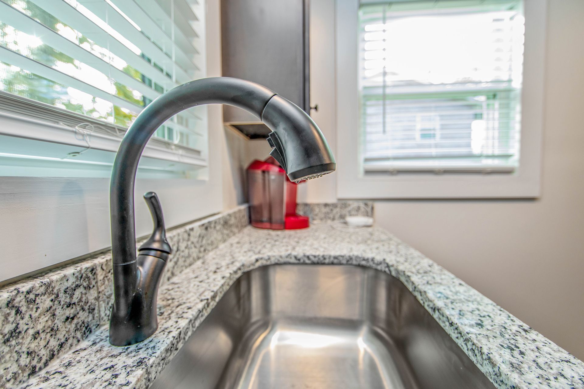 A kitchen sink with a black faucet and a window in the background.