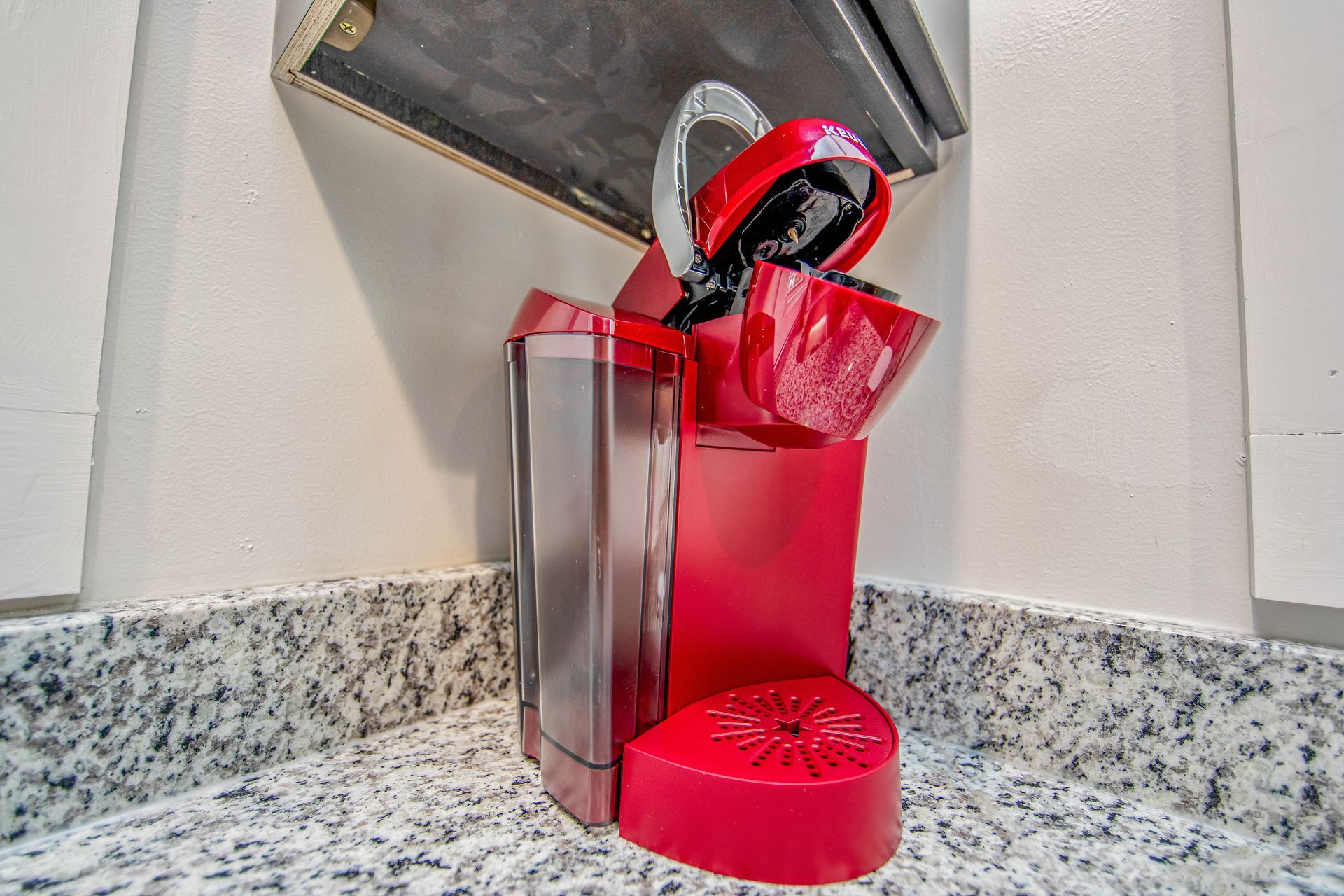 A red coffee maker is sitting on a granite counter.