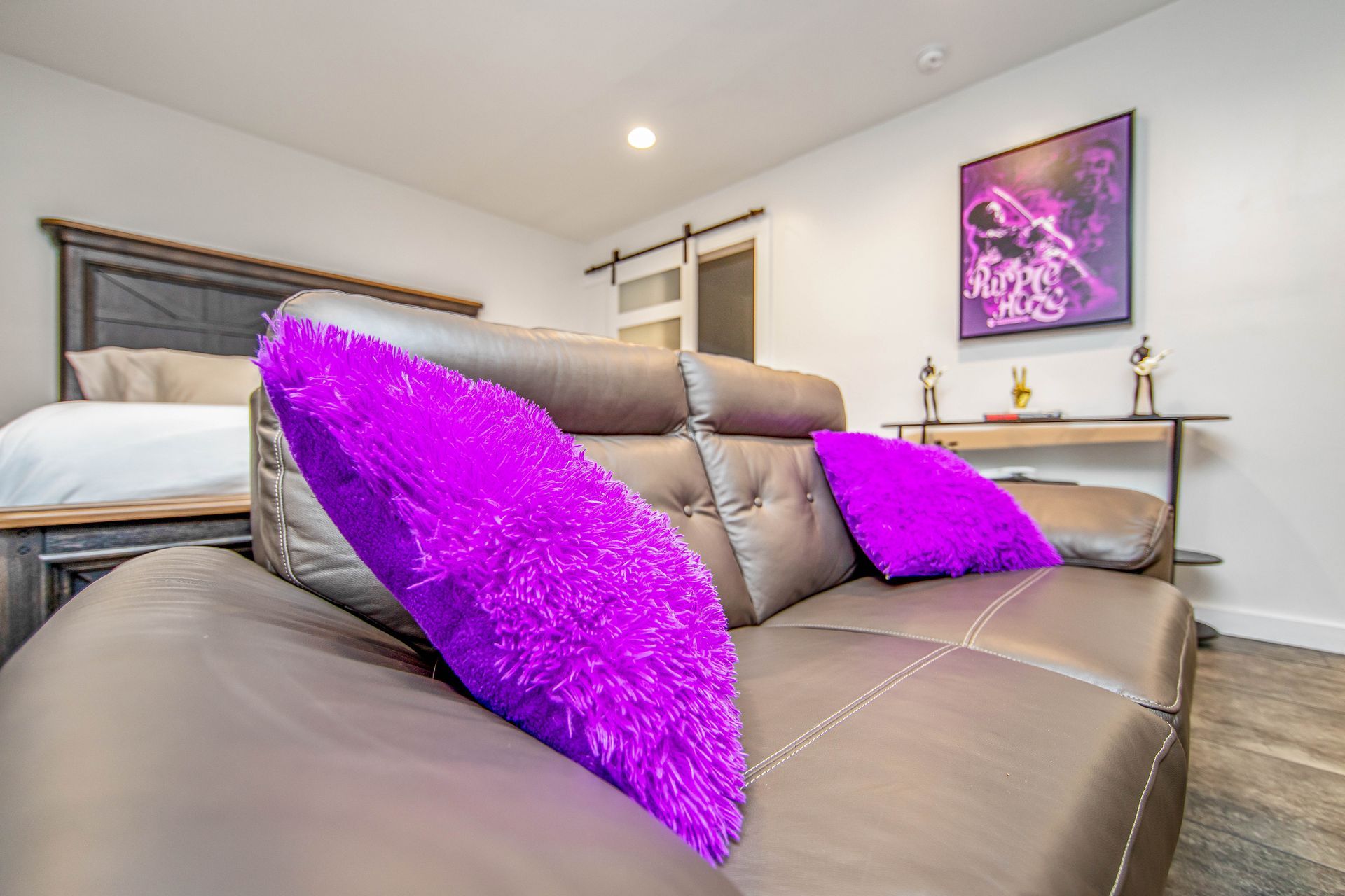 A brown leather couch with purple pillows in a bedroom.