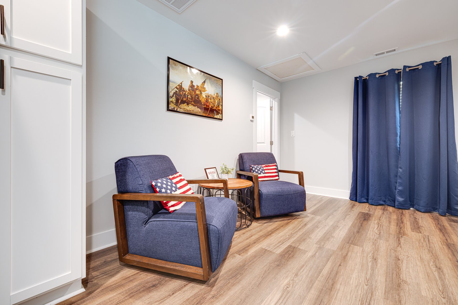 A living room with two chairs , a table and a painting on the wall.