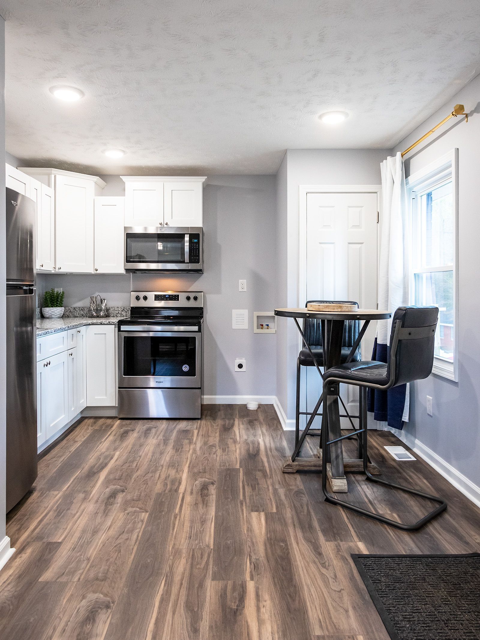 A kitchen with hardwood floors , stainless steel appliances , white cabinets and a table.