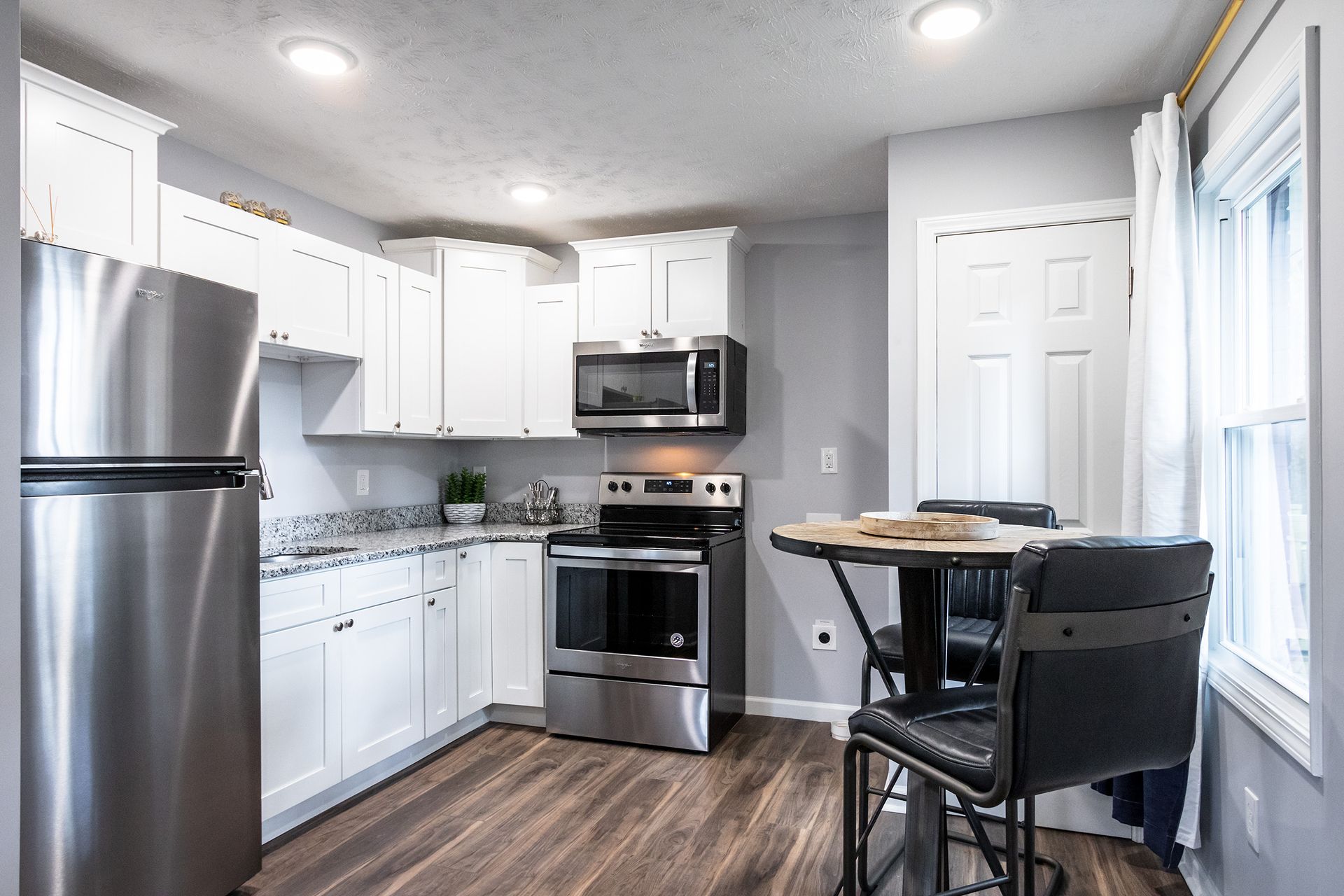 A kitchen with stainless steel appliances , white cabinets , a table and chairs.