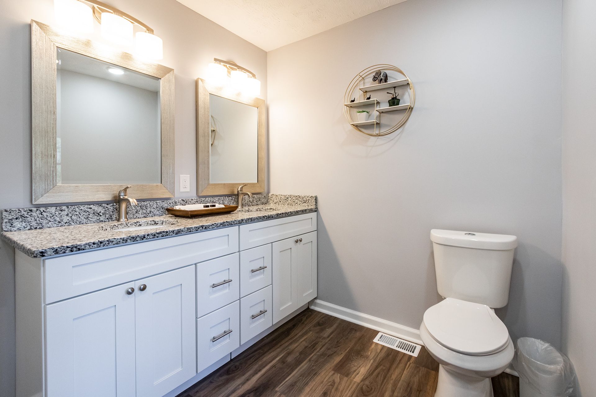 A bathroom with a toilet , sink , mirror and trash can.
