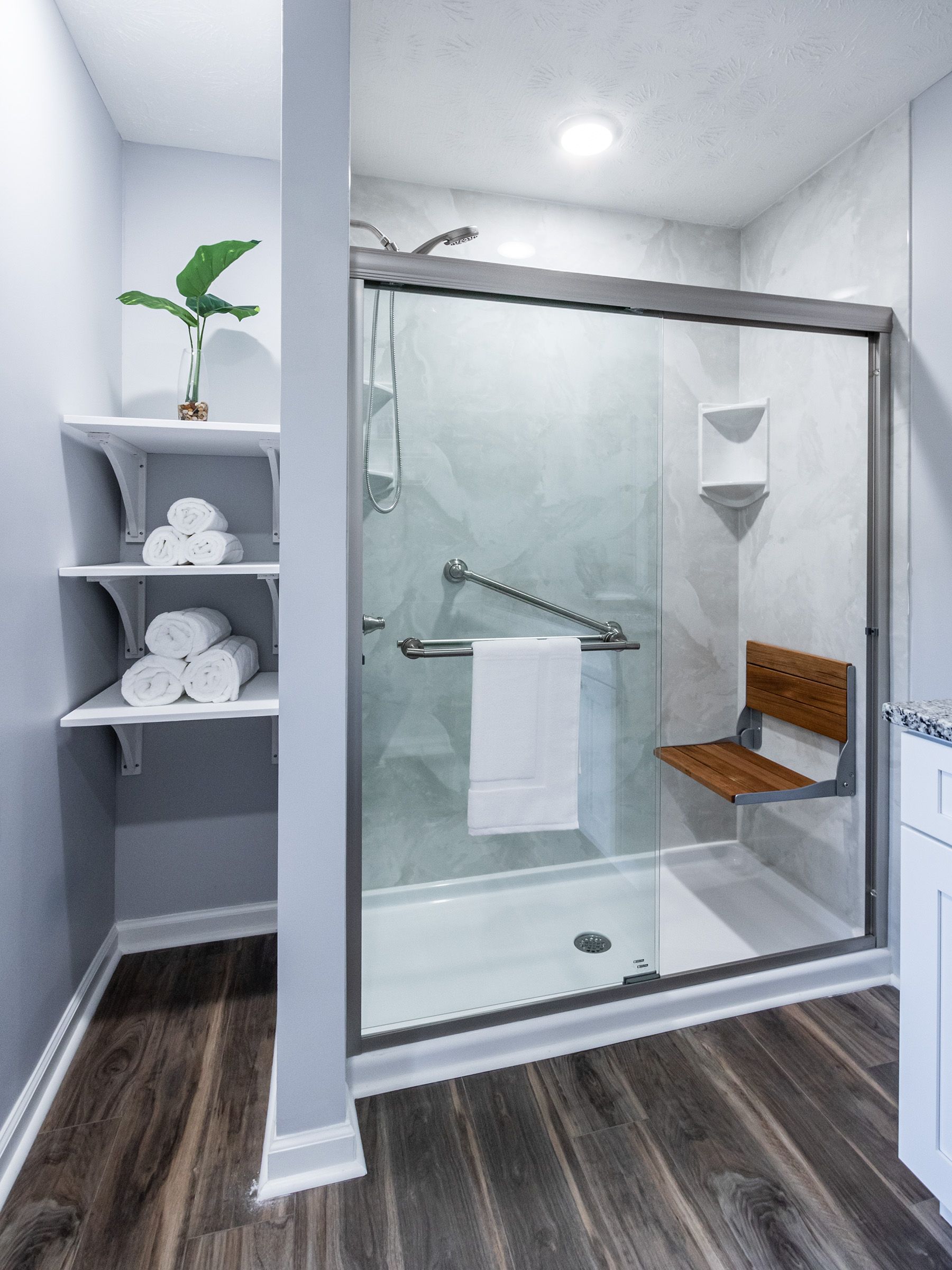 A bathroom with a sliding glass shower door and a wooden seat.
