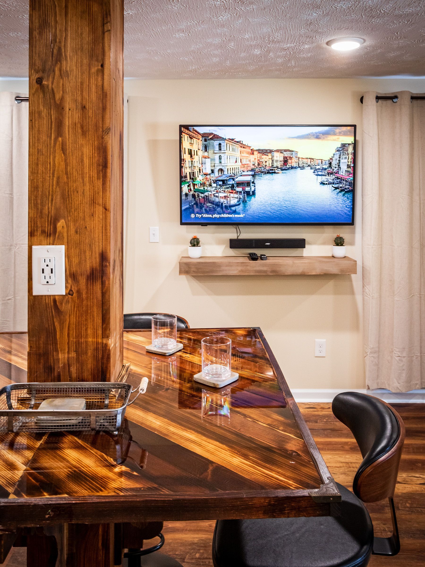 A living room with a wooden table and chairs and a flat screen tv on the wall.