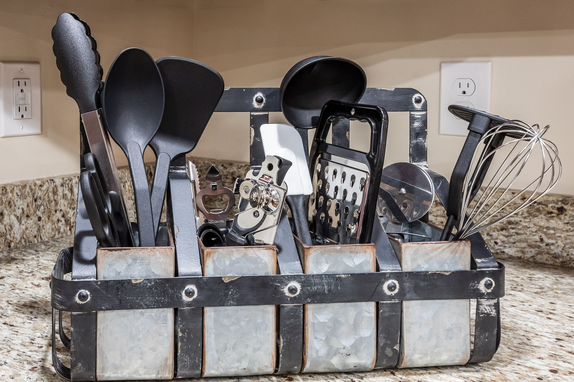 A basket filled with kitchen utensils is sitting on a counter.