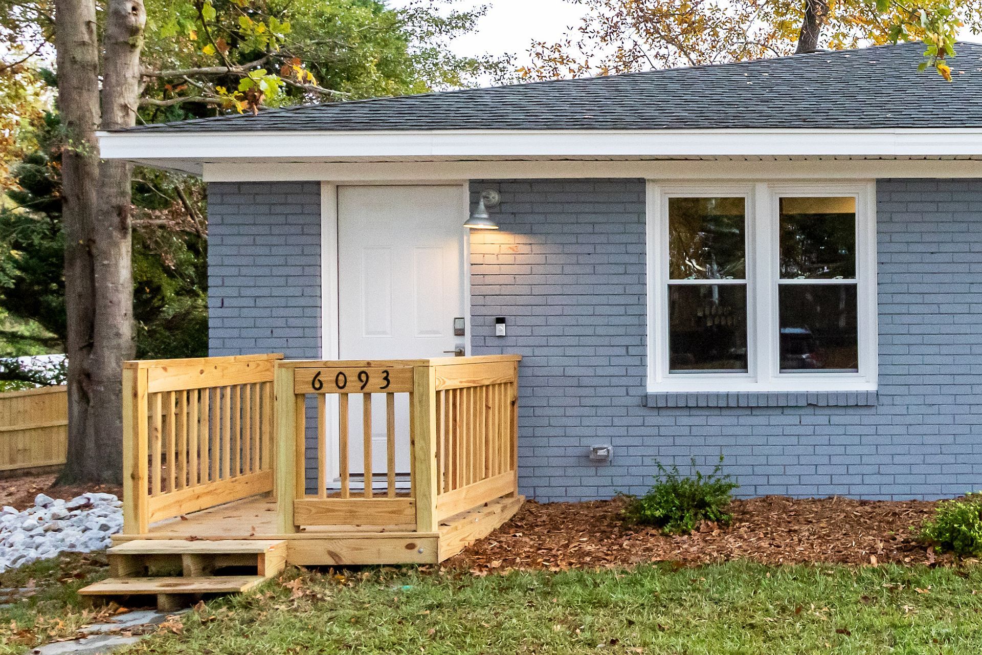 A small blue brick house with a wooden deck in front of it.