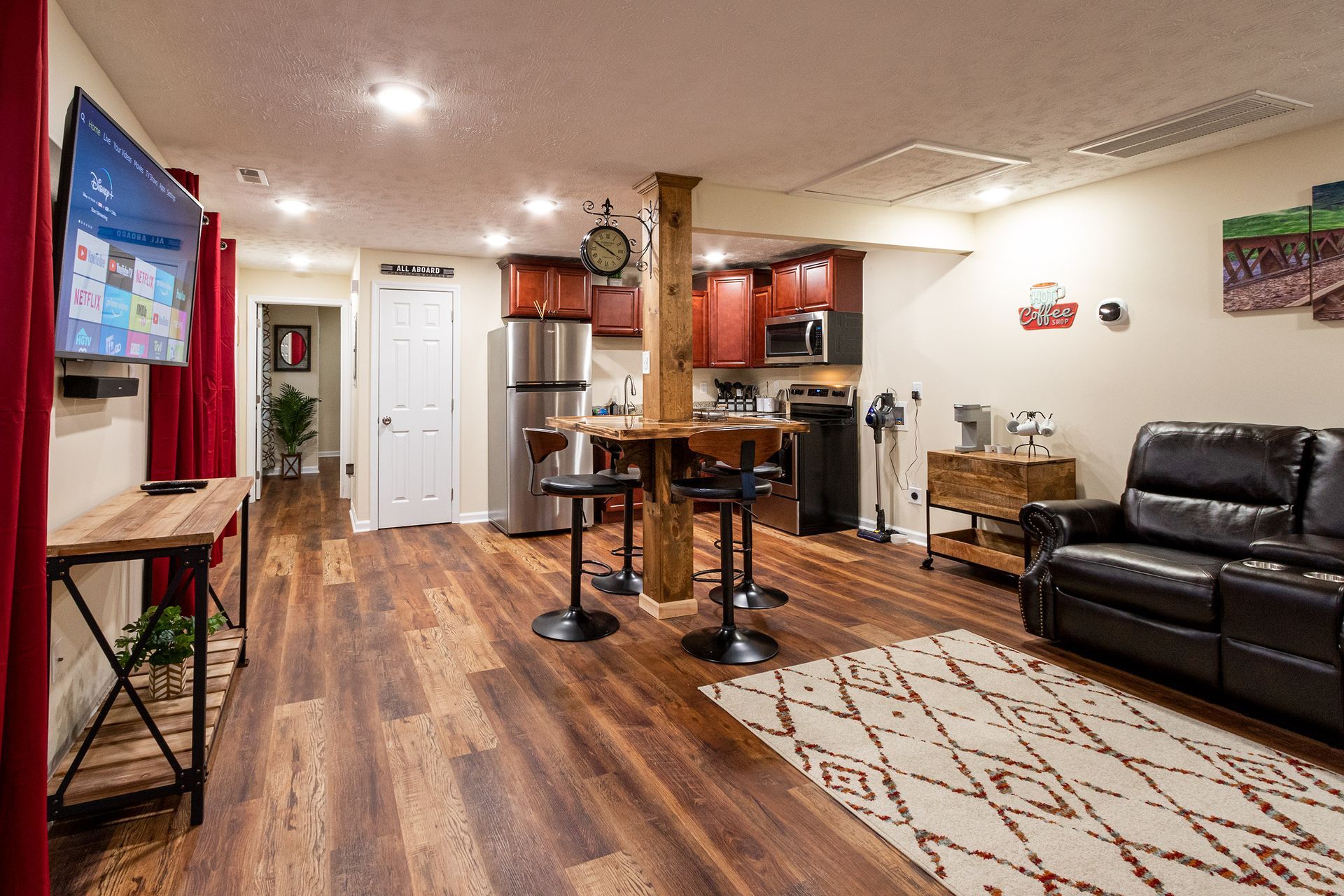 A living room with hardwood floors , a couch , a television and a kitchen.