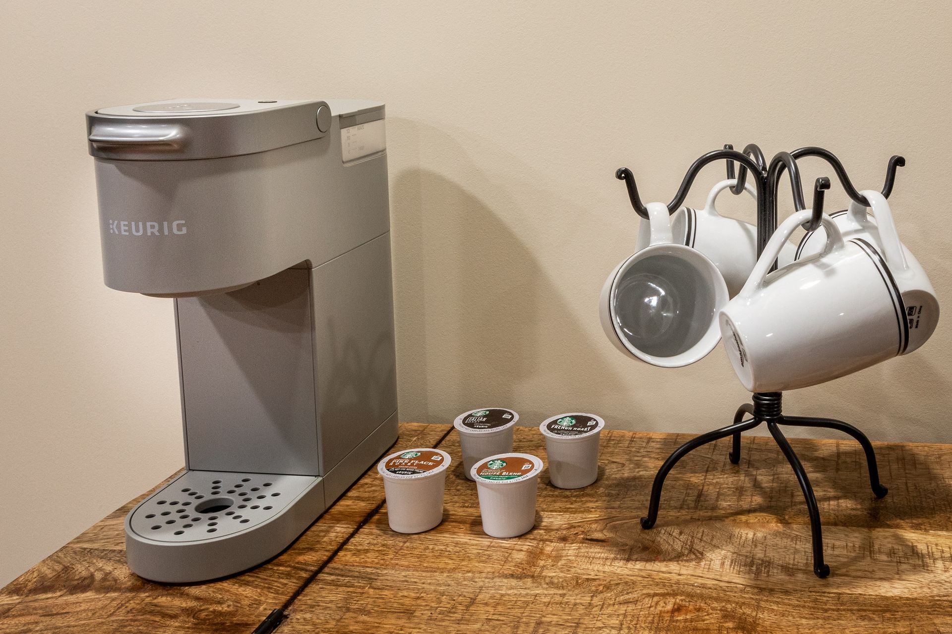 A keurig coffee maker and cups are sitting on a wooden table.