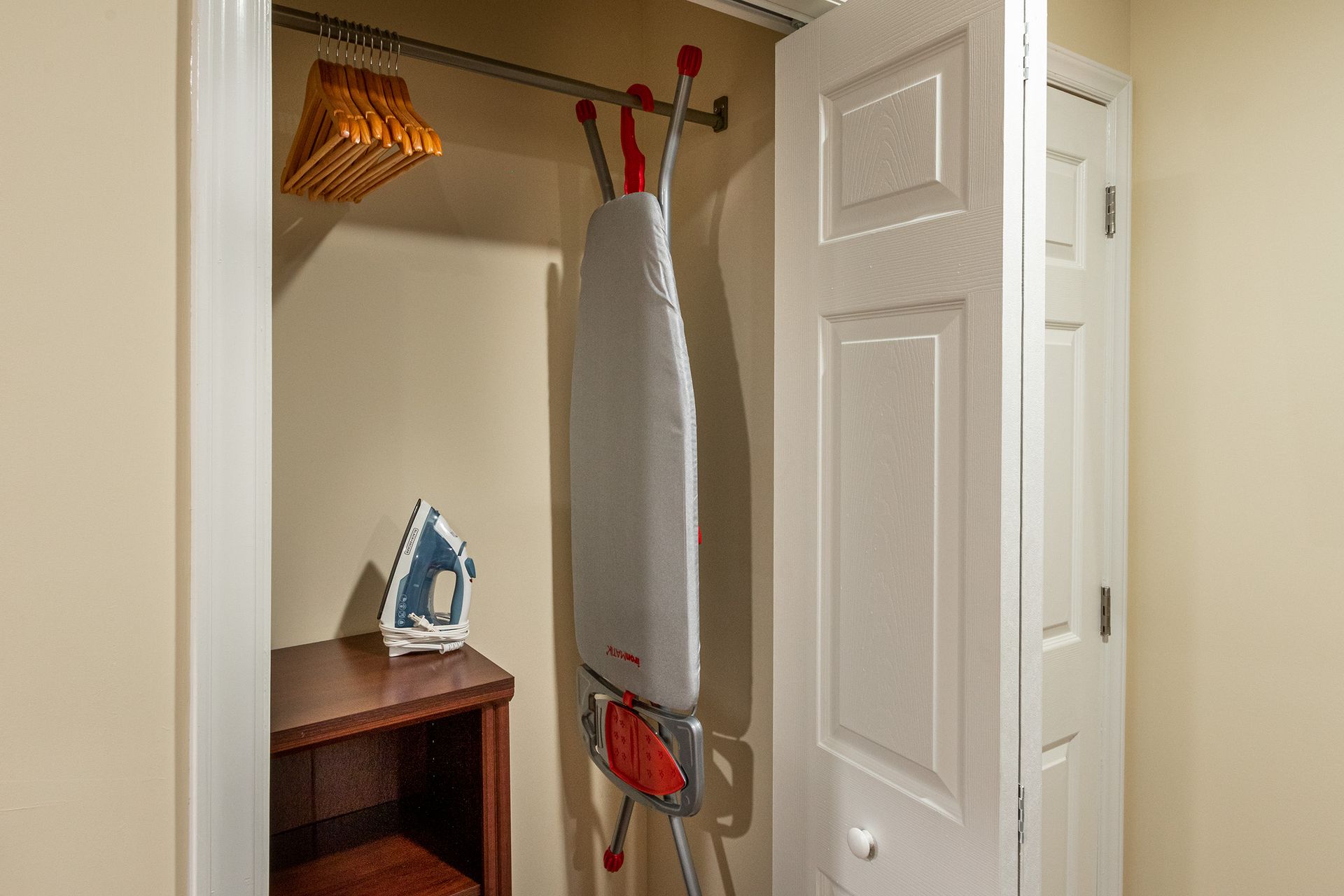 An ironing board is hanging in a closet next to a shelf.