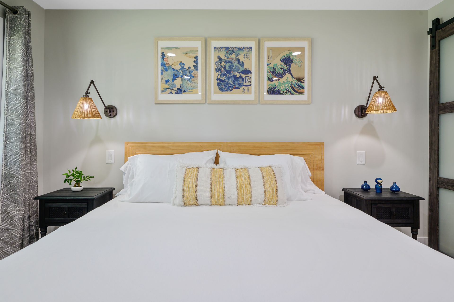 A bedroom with a king size bed , two nightstands , and three paintings on the wall.