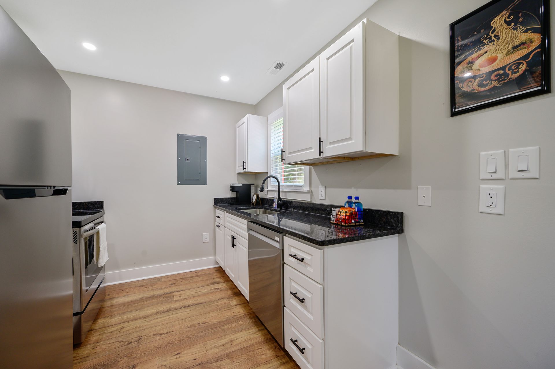 A kitchen with white cabinets , stainless steel appliances , hardwood floors and a picture on the wall.