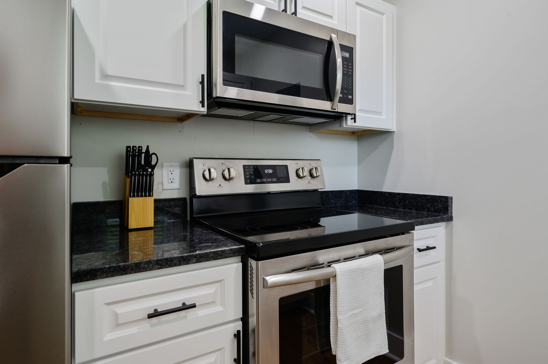 A kitchen with a stove , microwave , refrigerator and white cabinets.