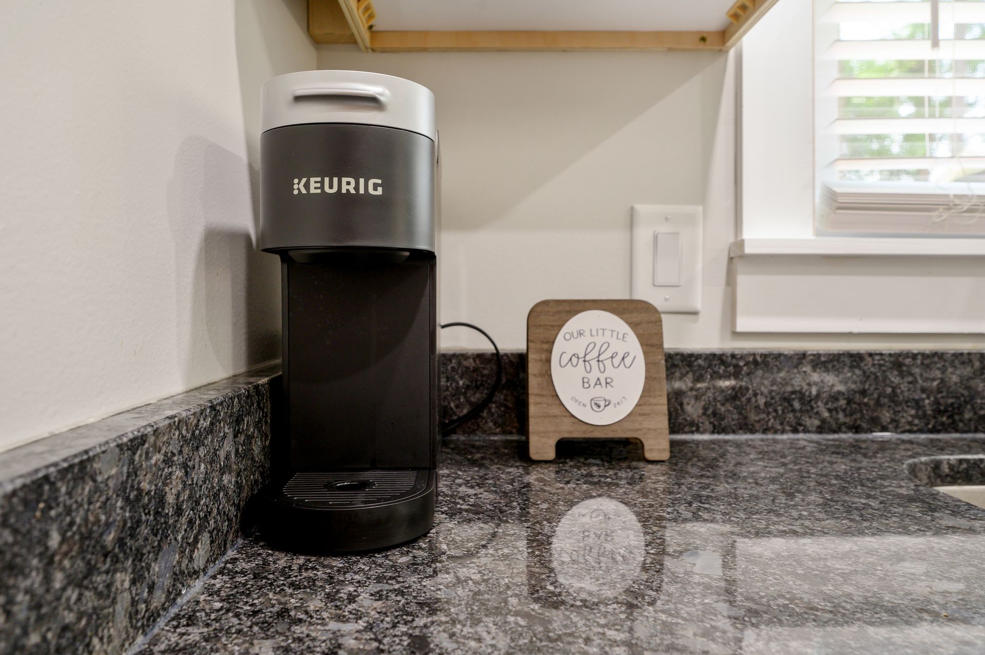 A keurig coffee maker is sitting on a kitchen counter next to a window.
