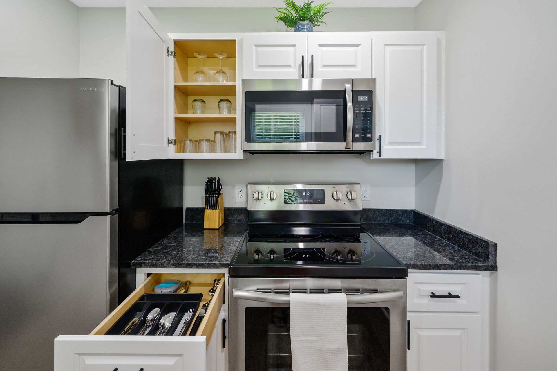 A kitchen with a stove , microwave , refrigerator and white cabinets.