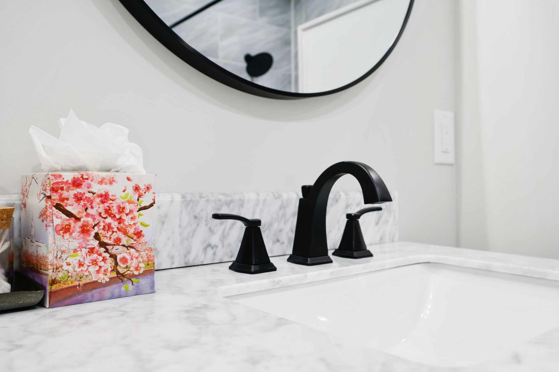 A bathroom sink with a round mirror and a box of tissues.
