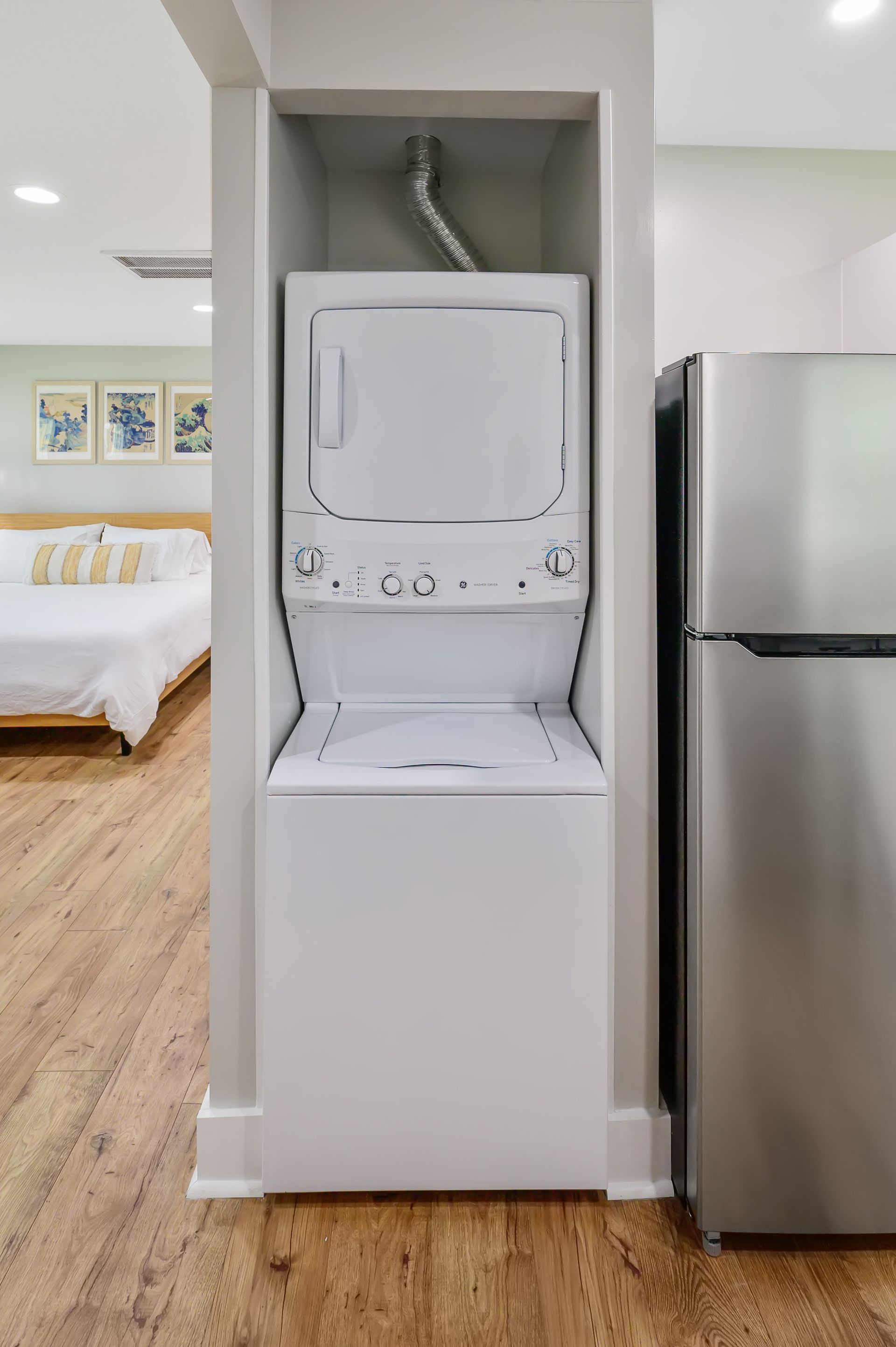A washer and dryer are stacked on top of each other in a kitchen next to a refrigerator.