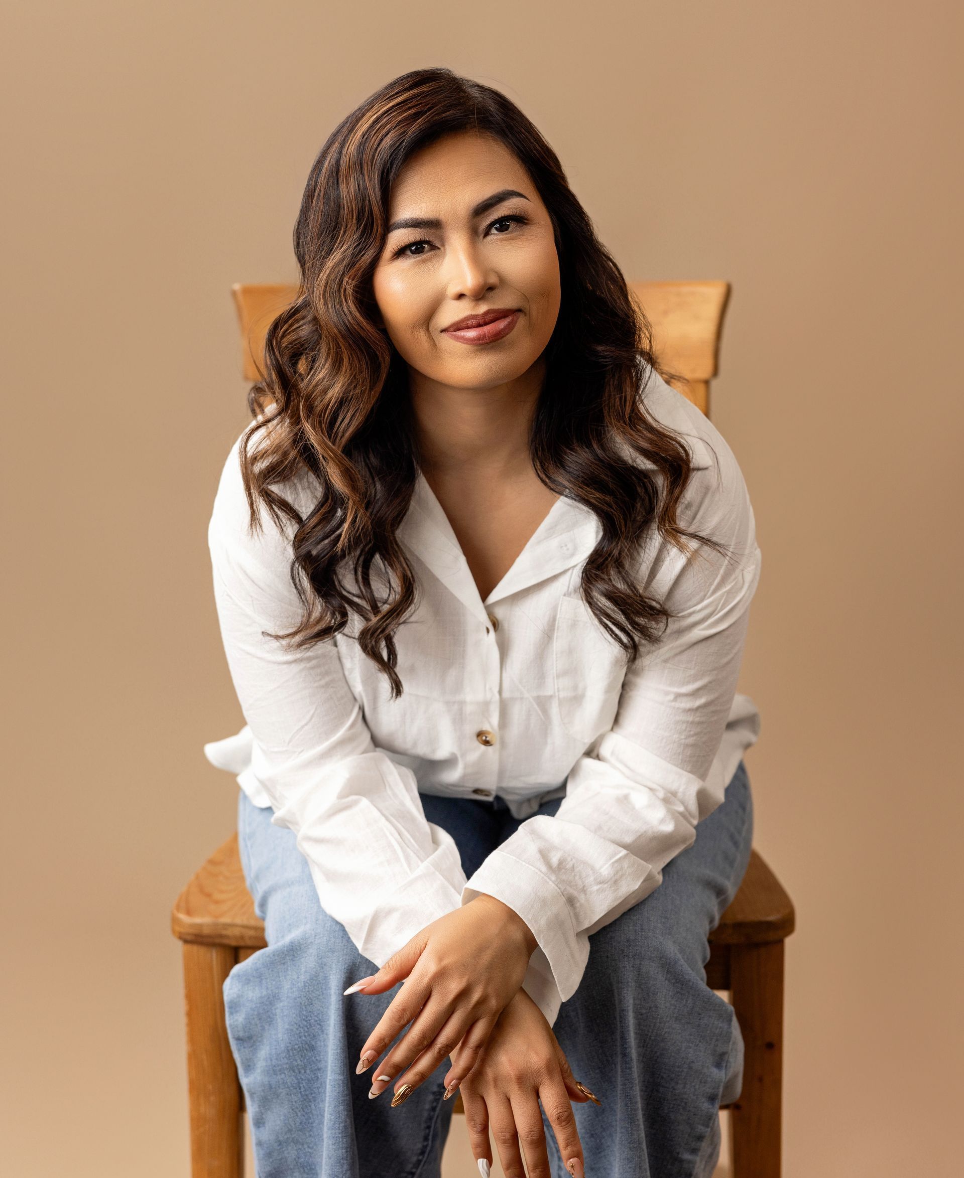 A woman is sitting on a wooden chair with her hands folded.