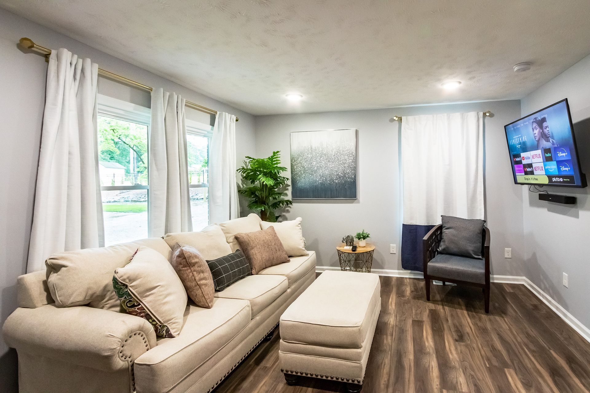 A living room with a couch , chair , ottoman and television.