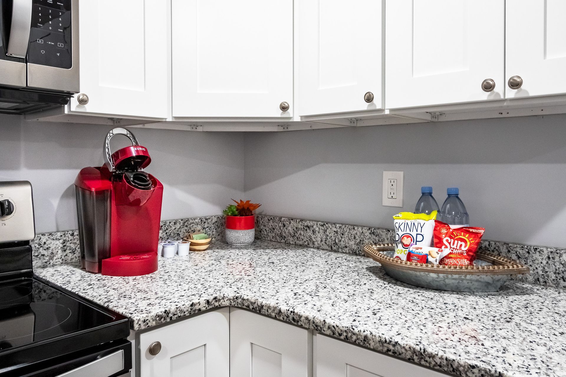 A kitchen with granite counter tops , stainless steel appliances , white cabinets and a red coffee maker.