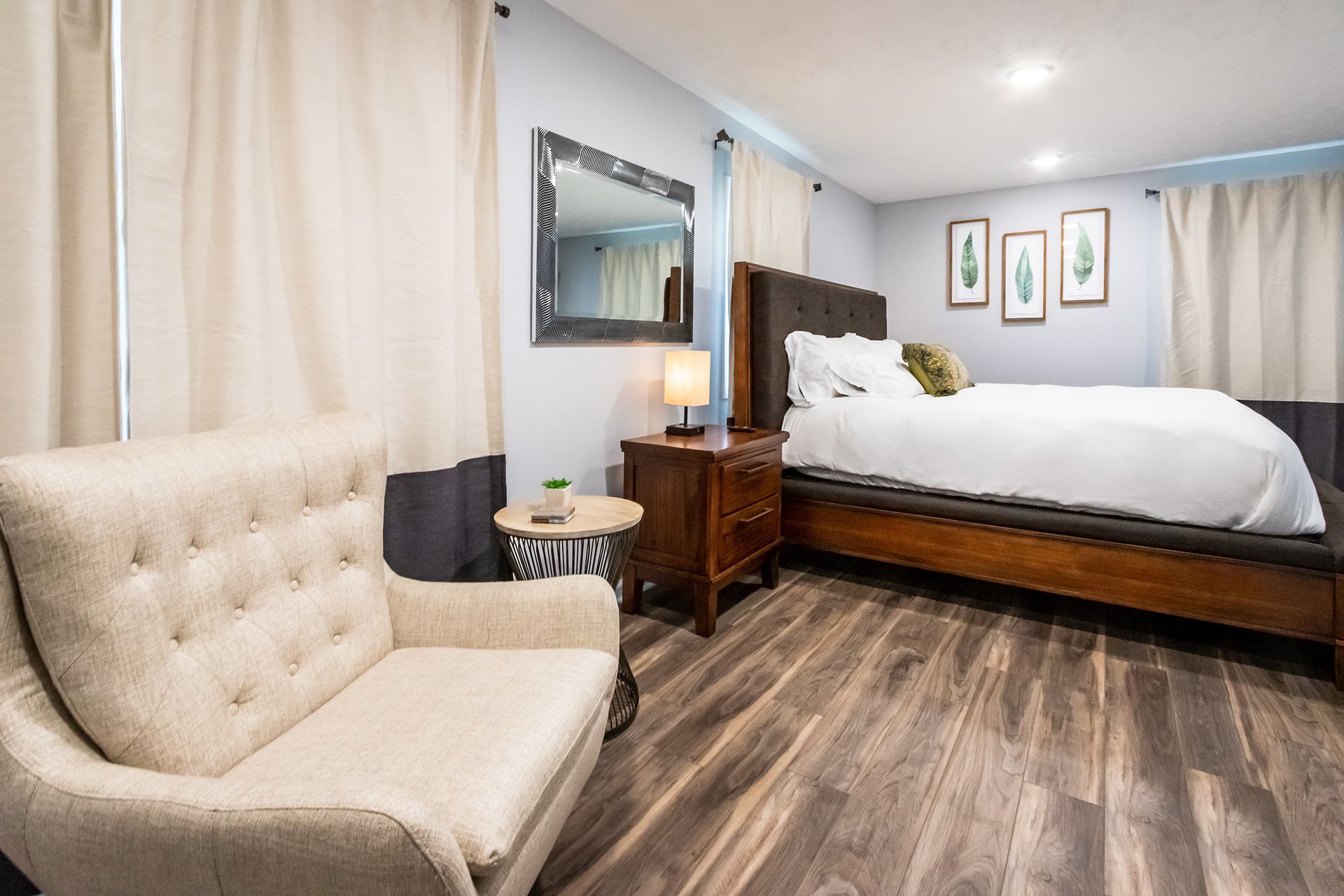 A bedroom with a bed , chair , nightstand and mirror.