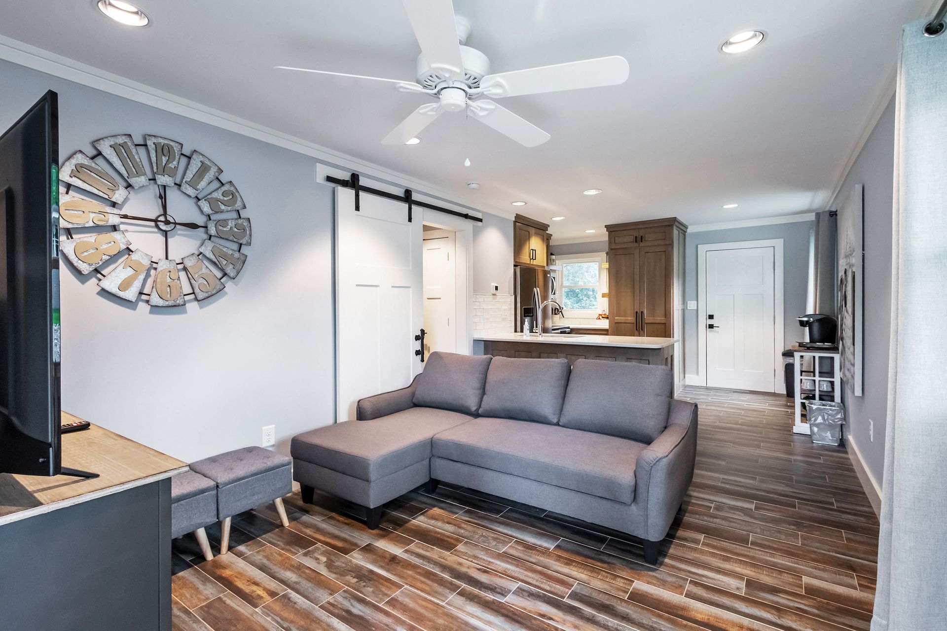 A living room with a couch , television , and a clock on the wall.