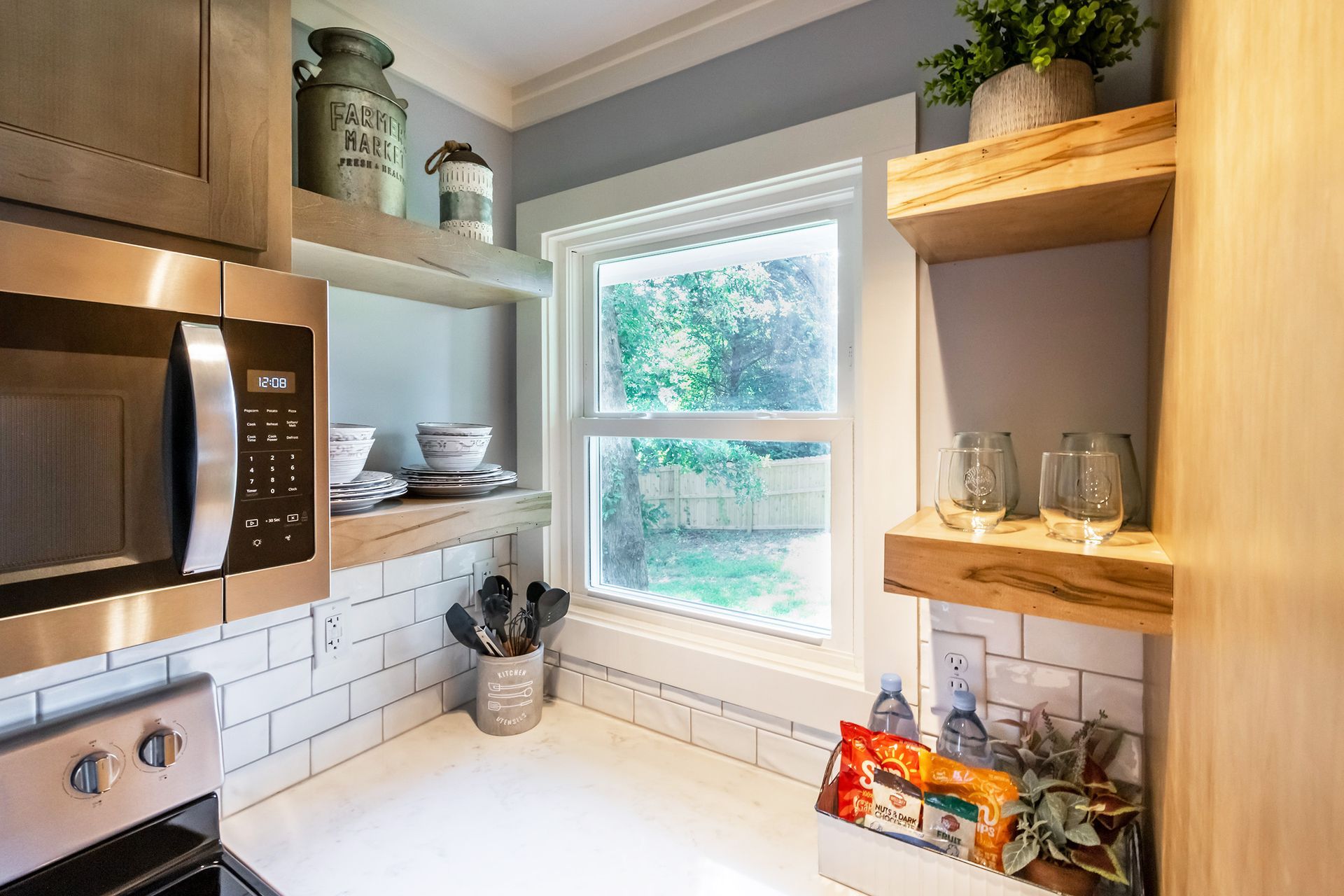 A kitchen with a stove , microwave , shelves and a window.