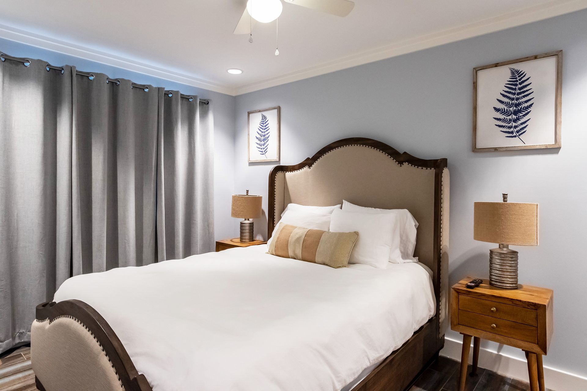 A bedroom with a bed , nightstands , lamps and a ceiling fan.