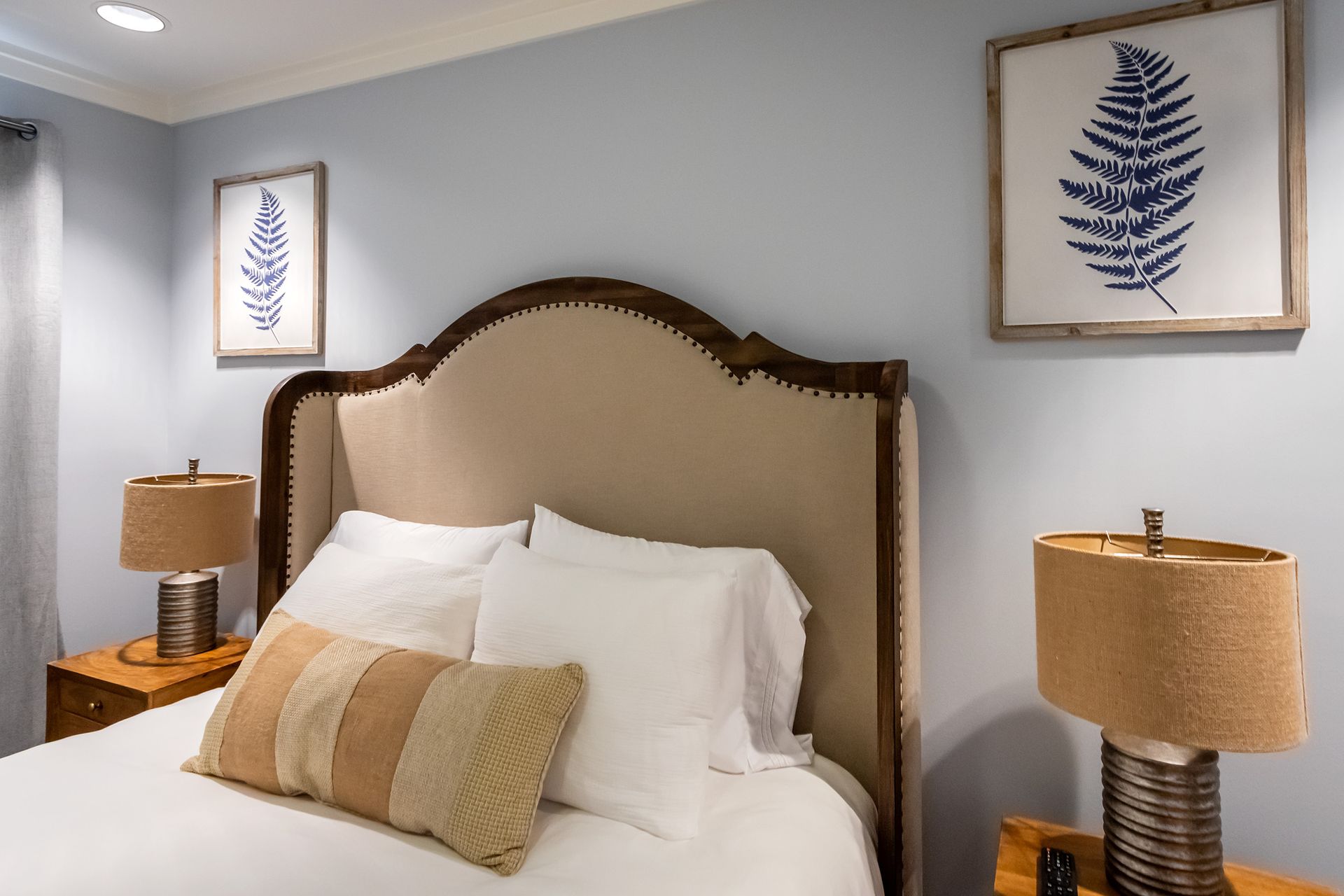 A bedroom with a bed , two lamps and two paintings on the wall.