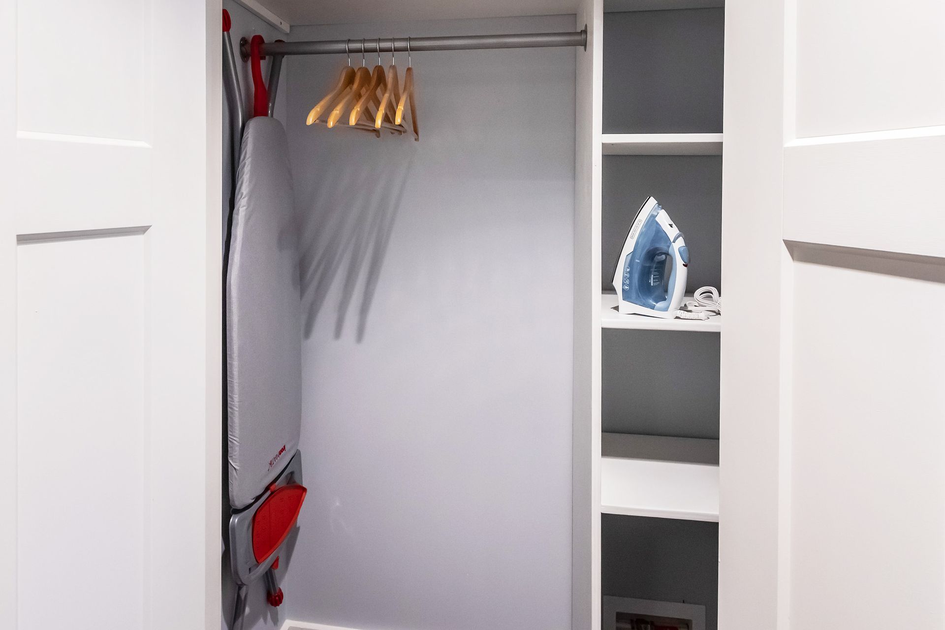 A closet with clothes hanging on a rack and an iron on a shelf.