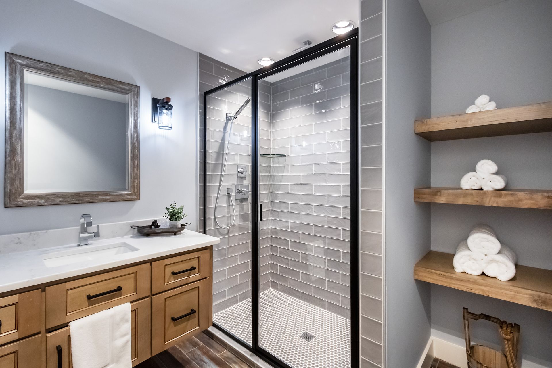 A bathroom with a walk in shower , sink , mirror and shelves.