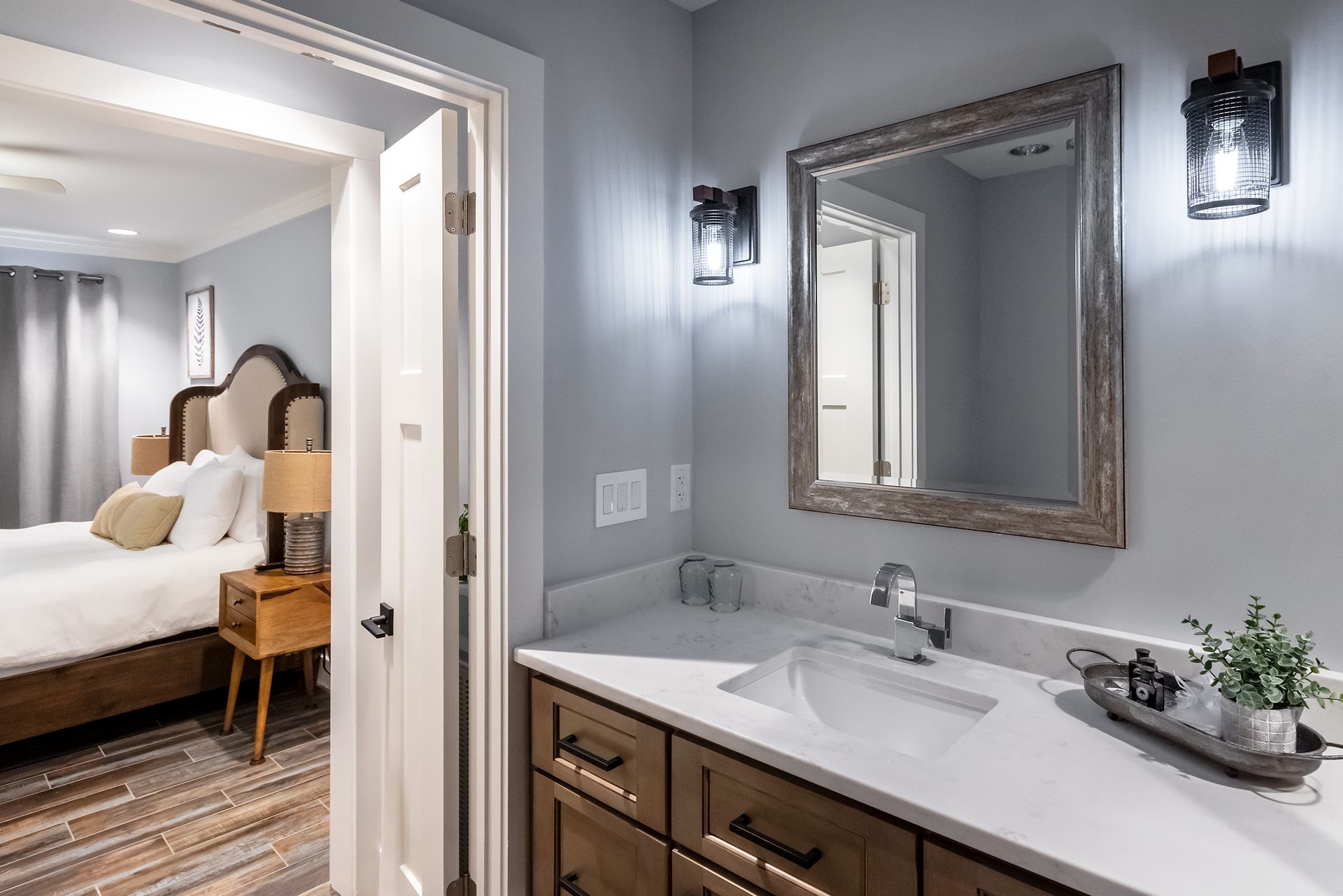 A bathroom with a sink and a mirror next to a bedroom.