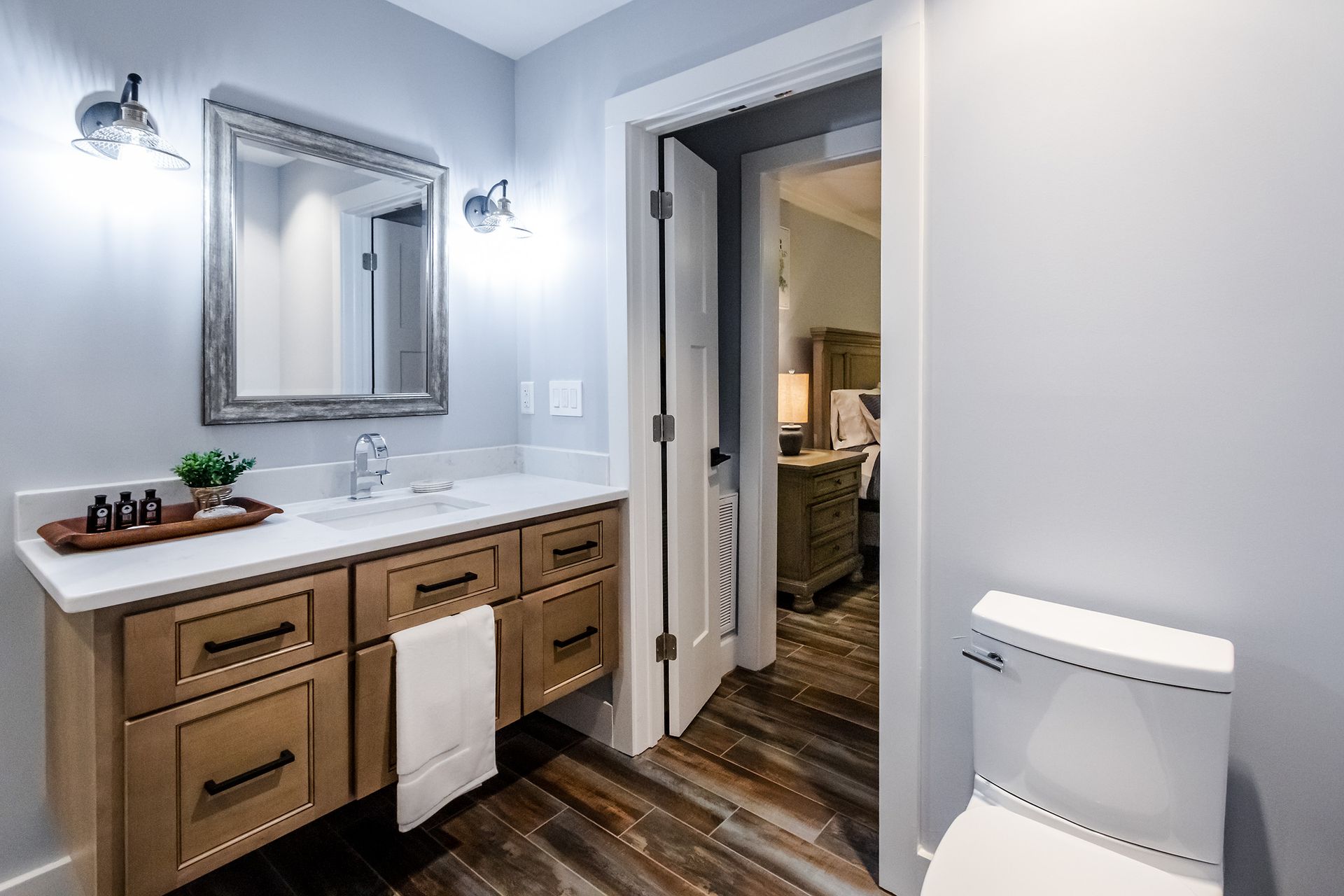 A bathroom with a sink , toilet , mirror and wooden cabinets.