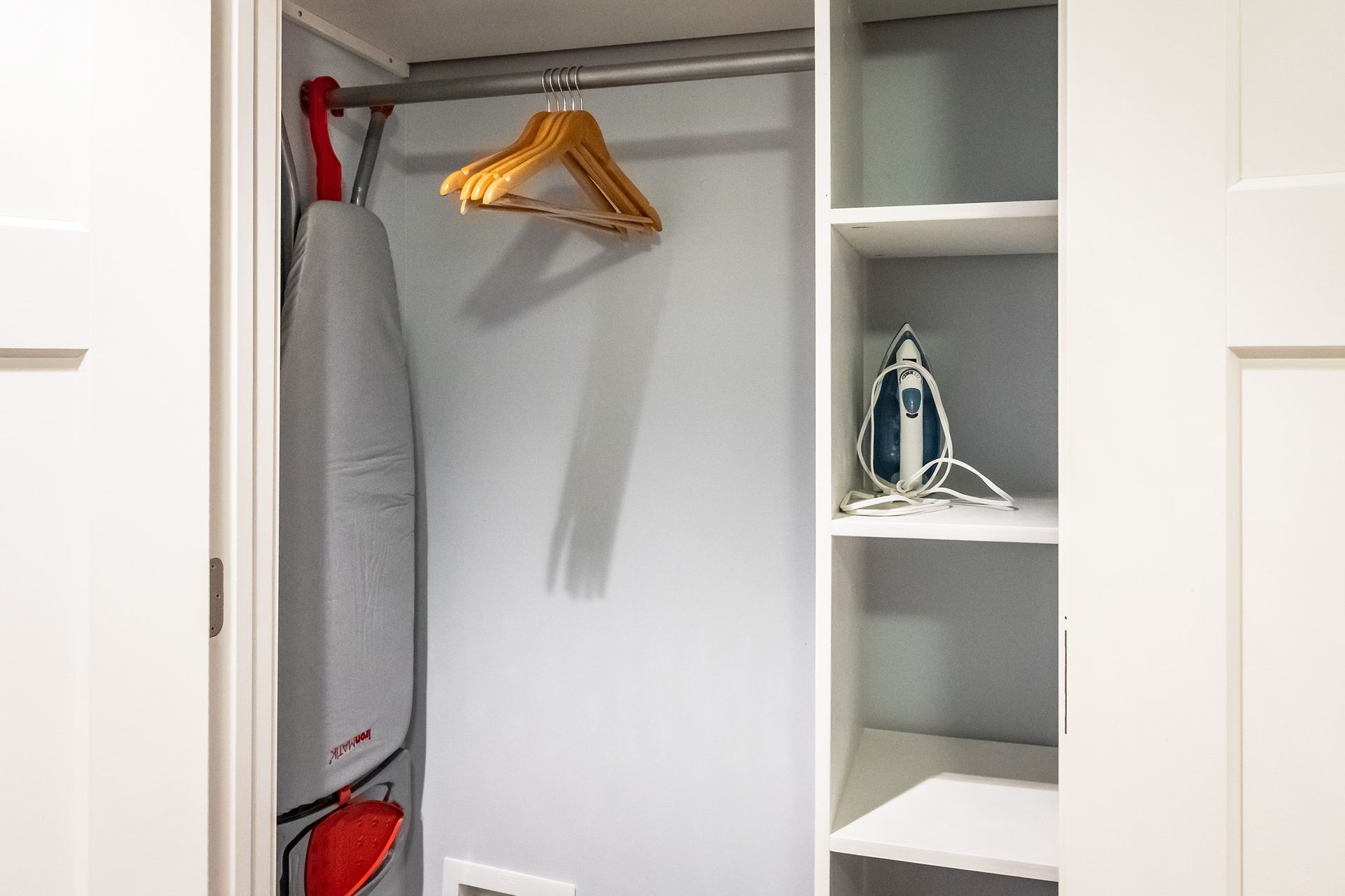 An ironing board is hanging in a closet next to a shelf.