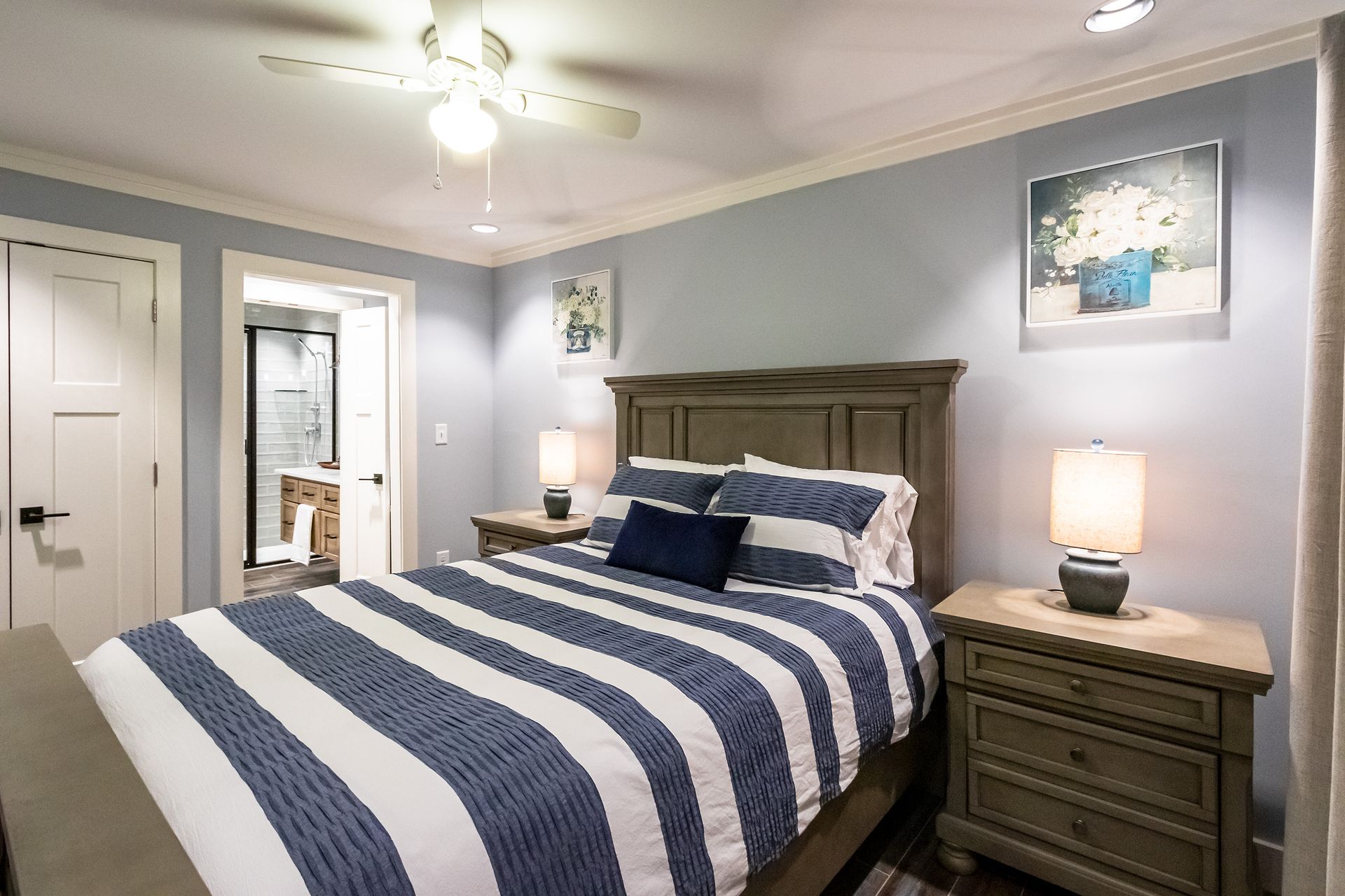 A bedroom with a king size bed , nightstands , lamps and a ceiling fan.