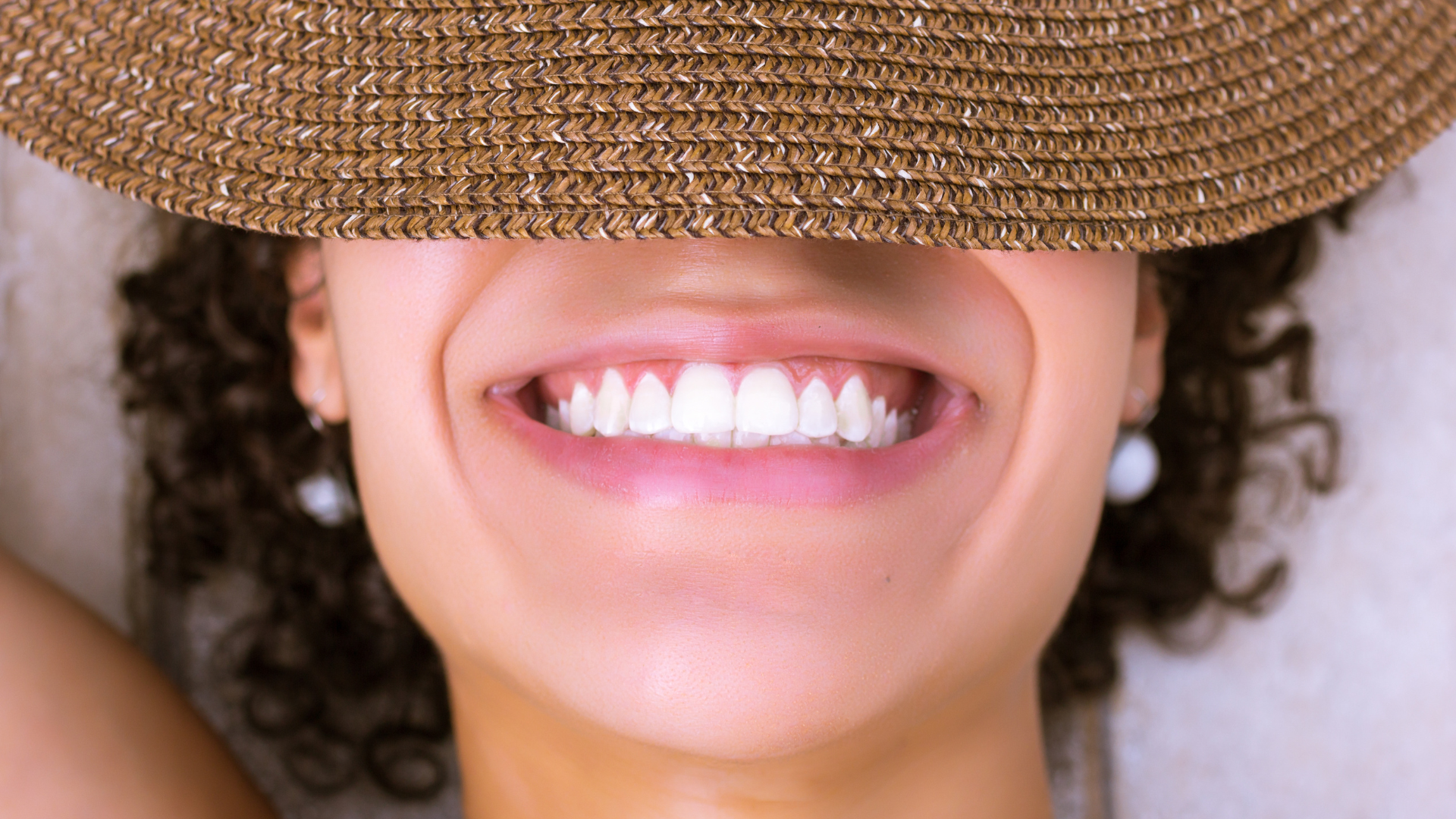 A woman with curly hair is laughing with her mouth open in a park.