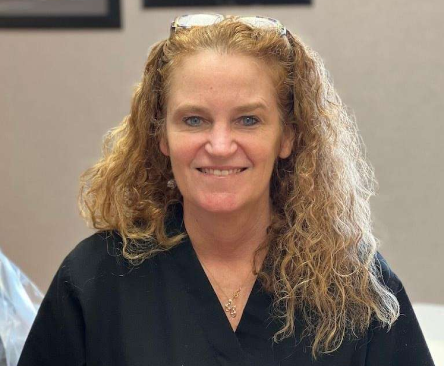 A woman wearing sunglasses and a black scrub top is smiling for the camera.