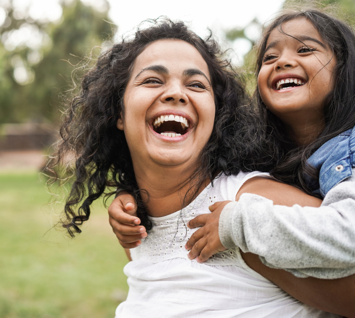 A woman is carrying a little girl on her back and they are laughing.