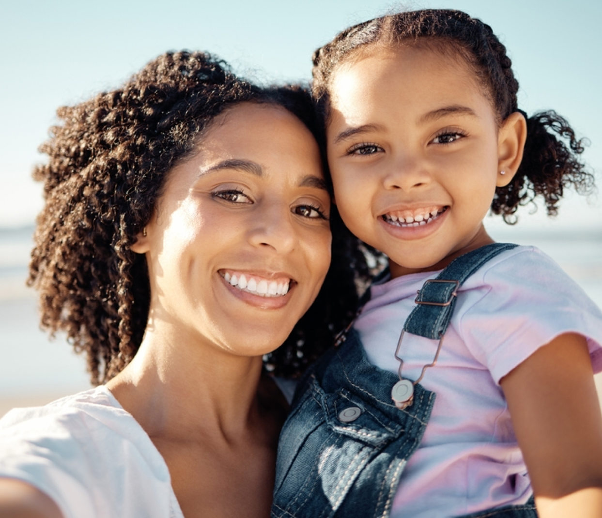 A woman is holding a little girl in her arms and they are smiling for the camera.