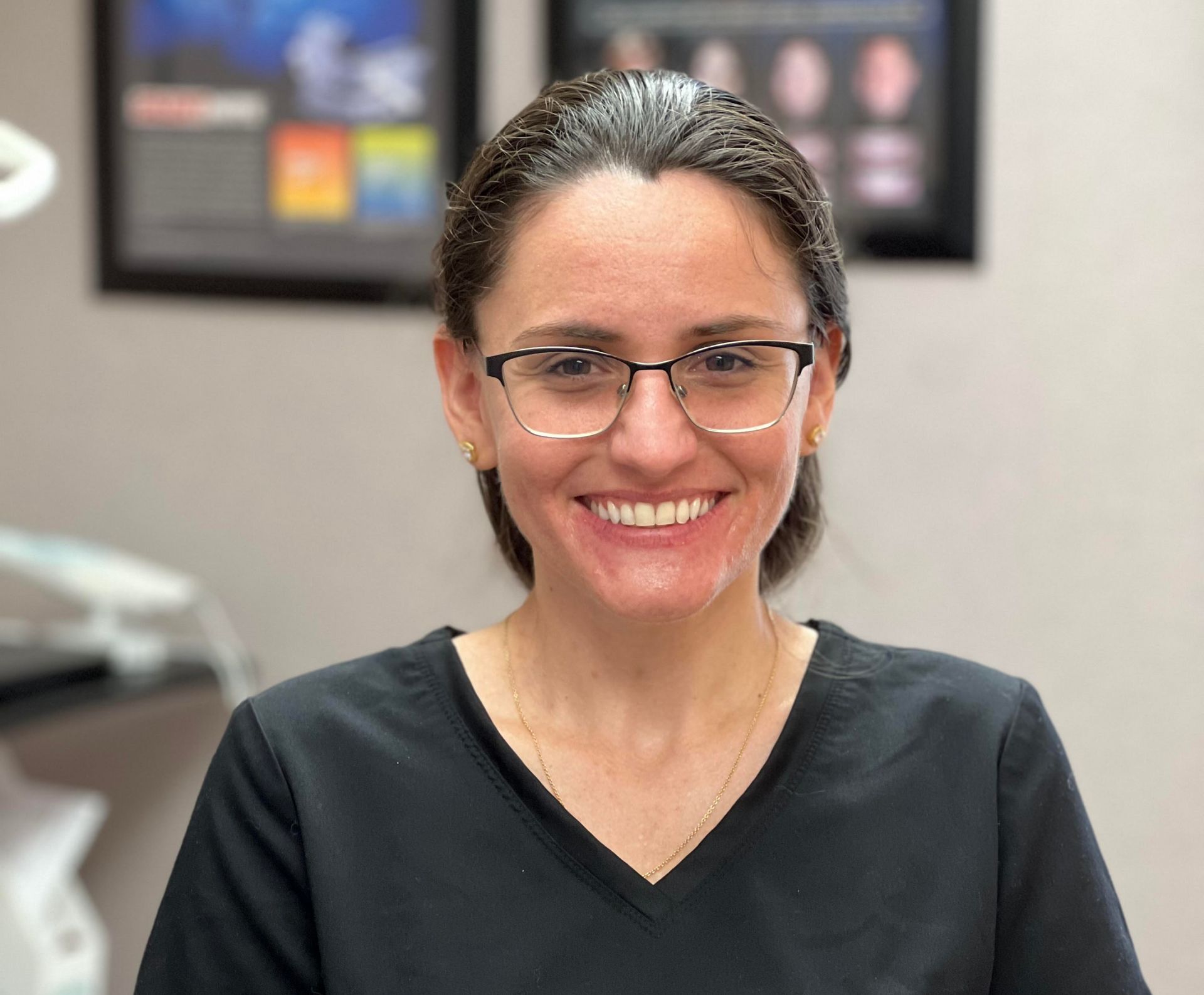 A woman wearing glasses and a black scrub top is smiling for the camera.