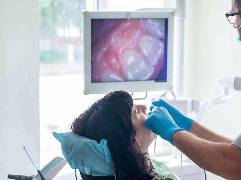 A woman is sitting in a dental chair while a dentist examines her teeth.