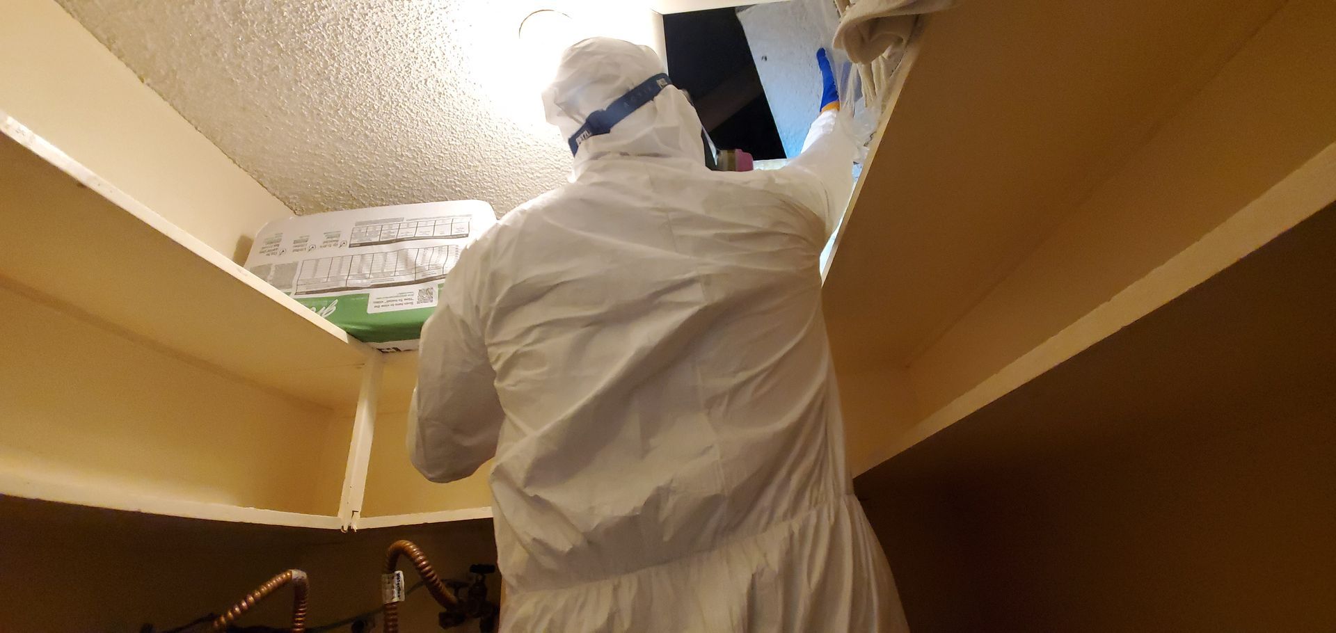 A man in a protective suit is cleaning the ceiling of a room.