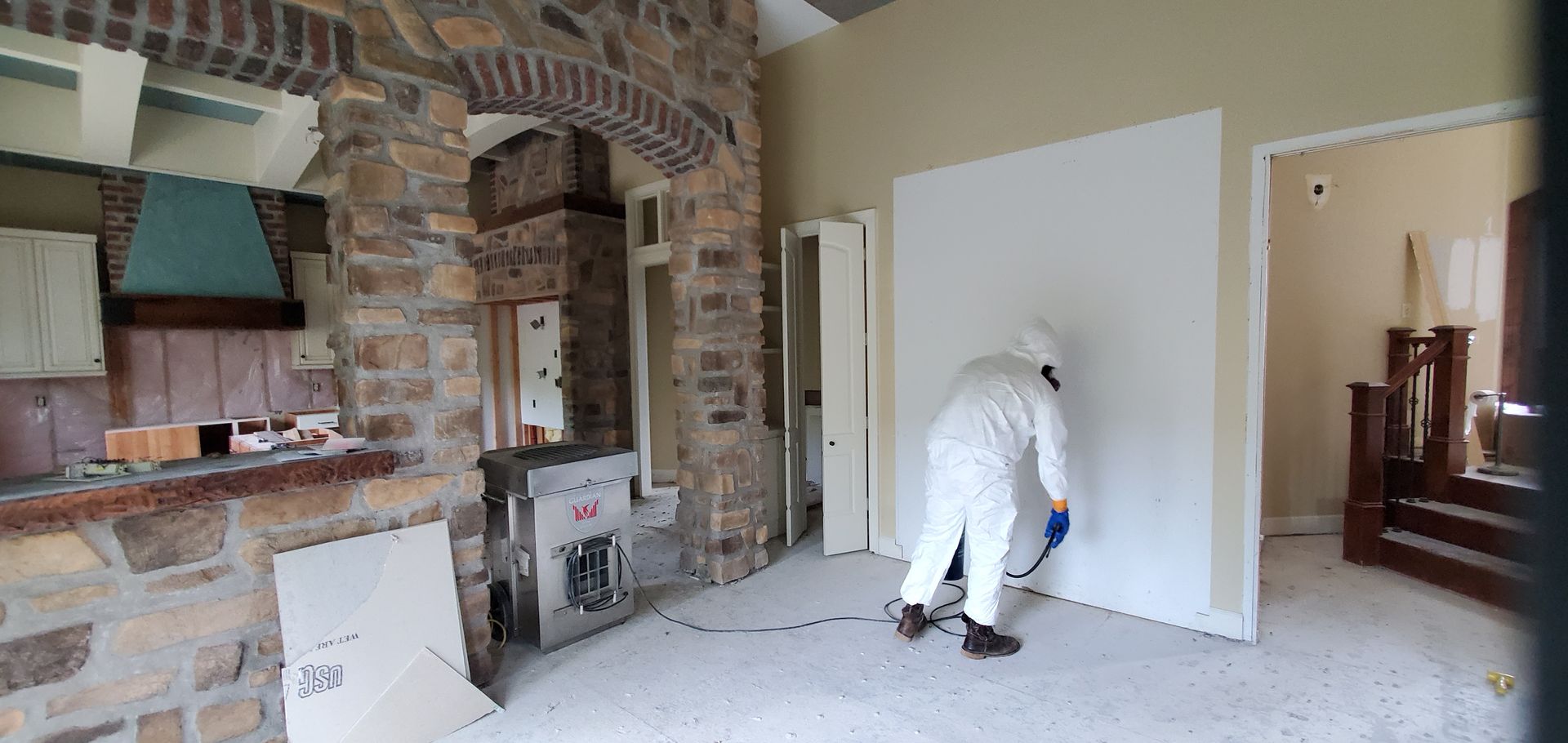 A man in a protective suit is cleaning a room in a house.